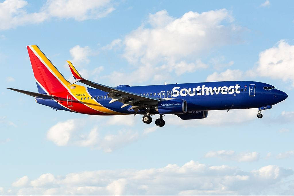 Plane 桌布 壁紙 — 一架西南航空的波音737，塗上鮮豔的藍、紅、黃色，在點綴著蓬鬆白雲的明亮天空中翱翔。
