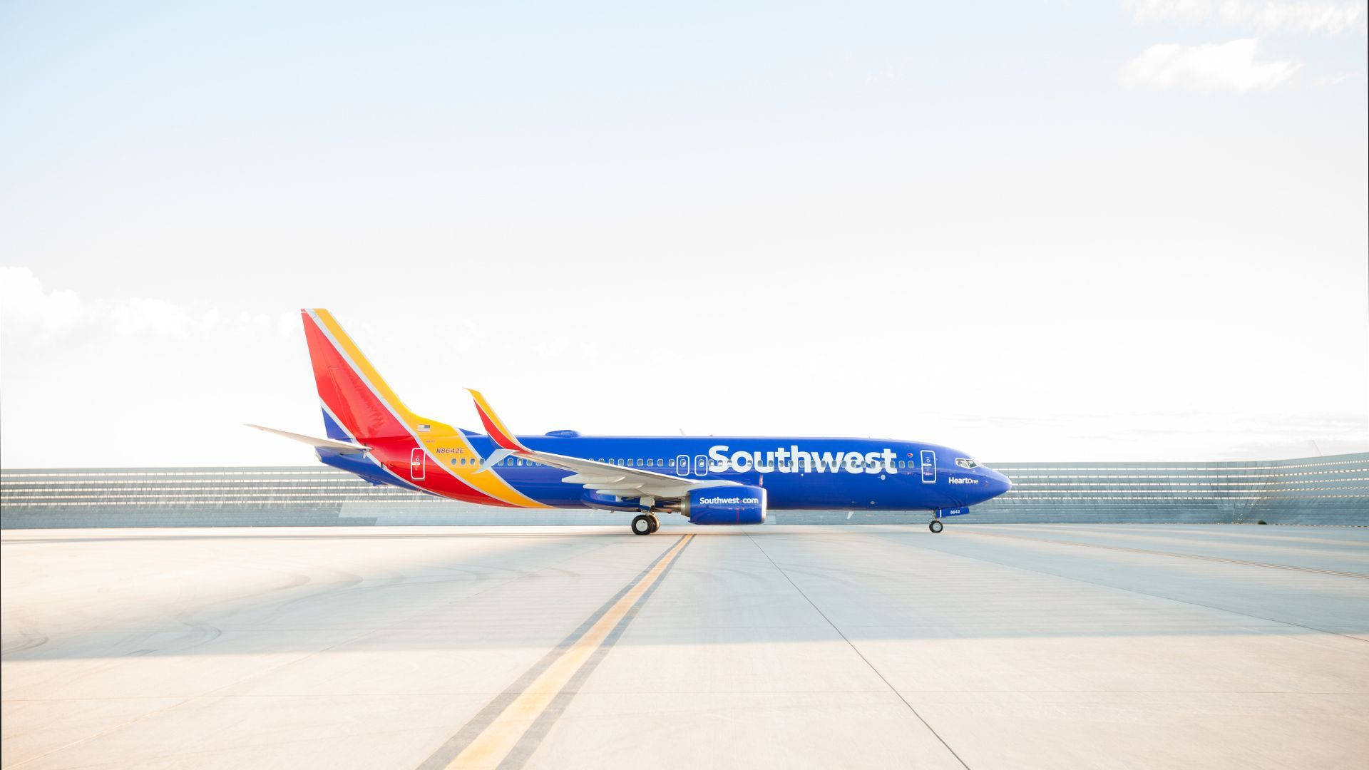 Southwest 桌布 壁紙 — 一架西南航空的飛機，採用鮮豔的藍、紅、黃色塗裝，停在陽光普照的機場停機坪上，背景是現代化的航廈。