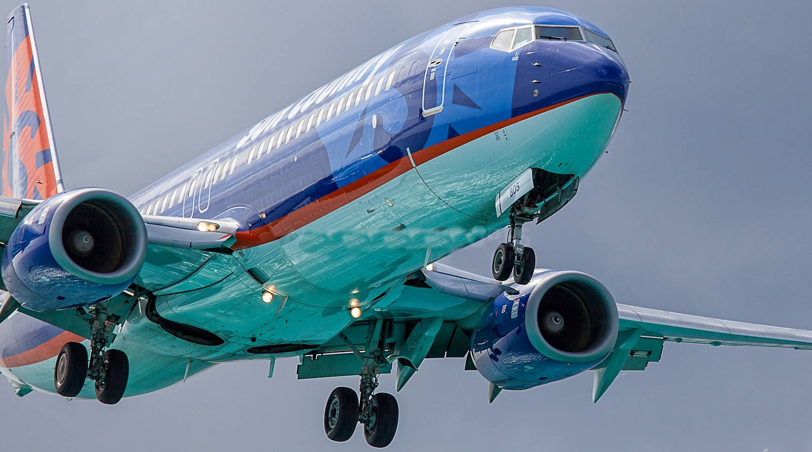 飛機 桌布 壁紙 — 一架西南航空的飛機以鮮豔的藍綠色和橙色塗裝，在放下起落架的情況下，在陰天中急轉彎。