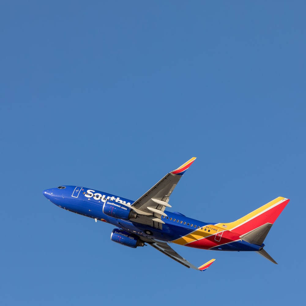 Southwest 桌布 壁紙 — 一架西南航空的飛機在清澈的藍天中翱翔，帶有鮮豔的紅、黃、藍色塗裝。
