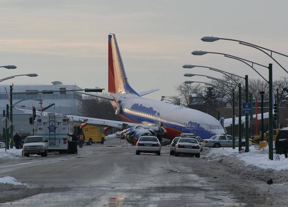 Road 桌布 壁紙 — 一架西南航空的飛機在黎明時分墜毀在積雪的機場道路上，周圍有應急車輛和汽車。
