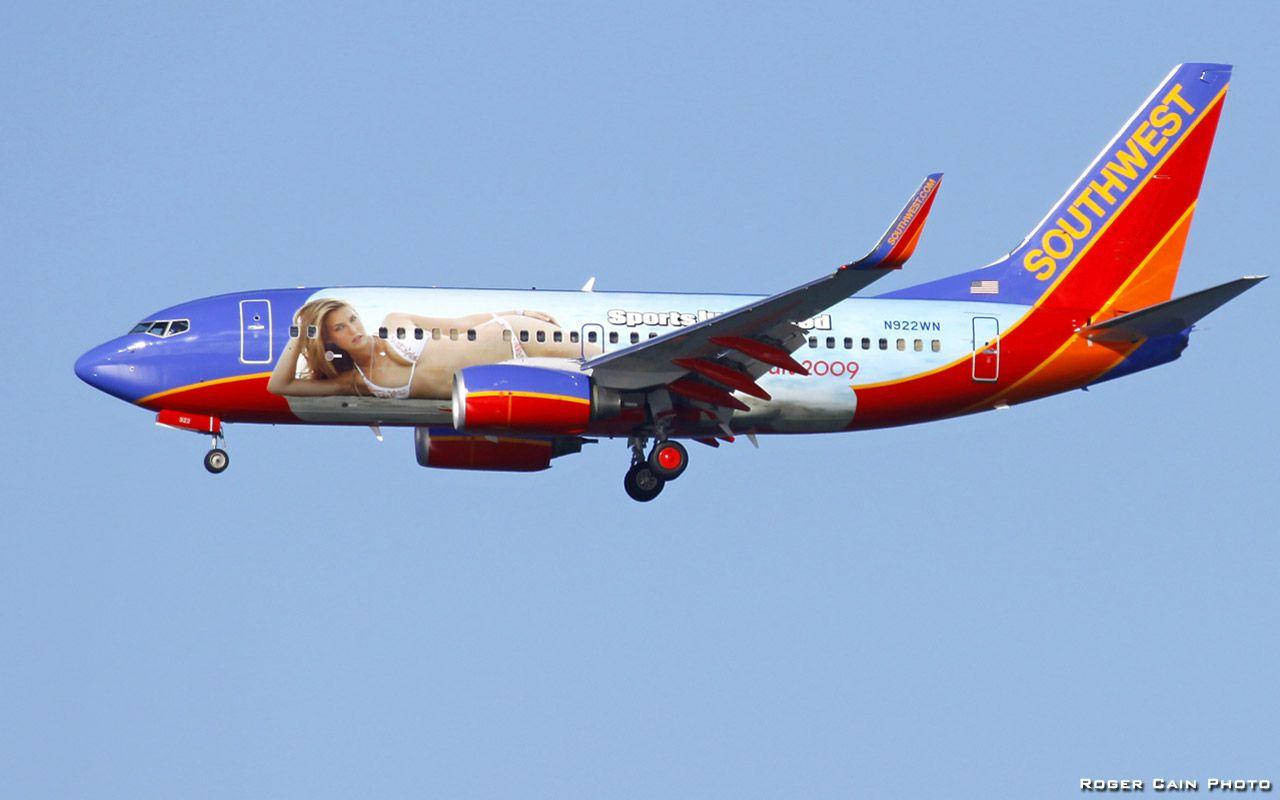 Southwest Airlines 桌布 壁紙 — 一架西南航空的飛機帶有大型女性廣告，在白天晴朗的藍天下飛行。