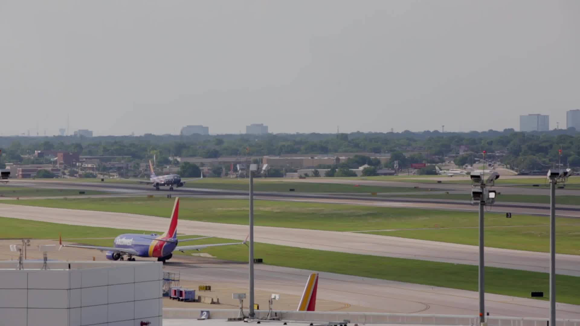 Airport 桌布 壁紙 — 一架西南航空飛機在霧濛濛的機場跑道上滑行，遠處有城市建築和綠色田野，天空多雲。