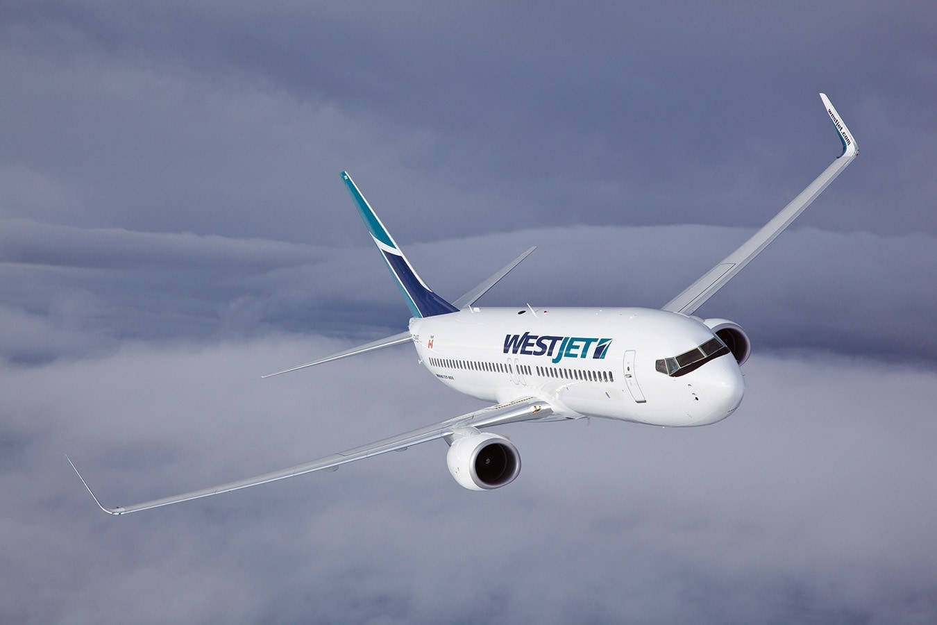  壁紙 — 一架西捷航空飛機在濃密灰色雲層上方翱翔，機翼向上傾斜，映襯著陰沉天空。