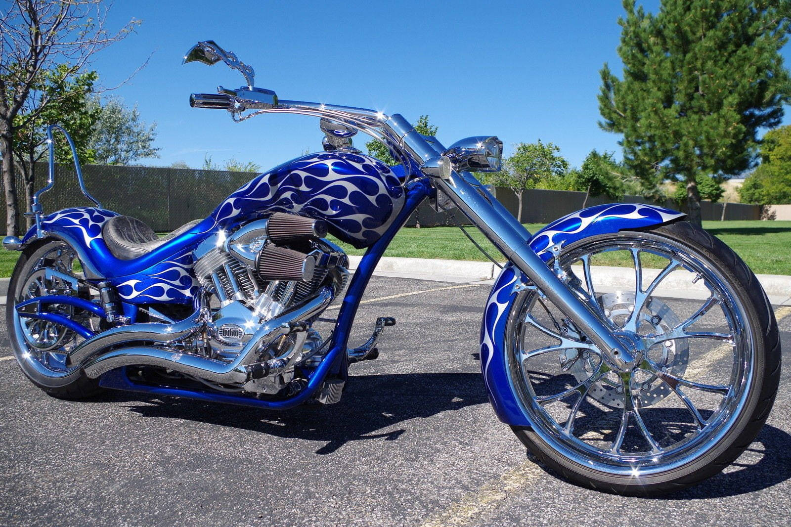 Bobber 桌布 壁紙 — 一架訂製的藍色火焰塗裝chopper機車，帶有鍍鉻裝飾，停放在晴朗藍天下的瀝青路面上。