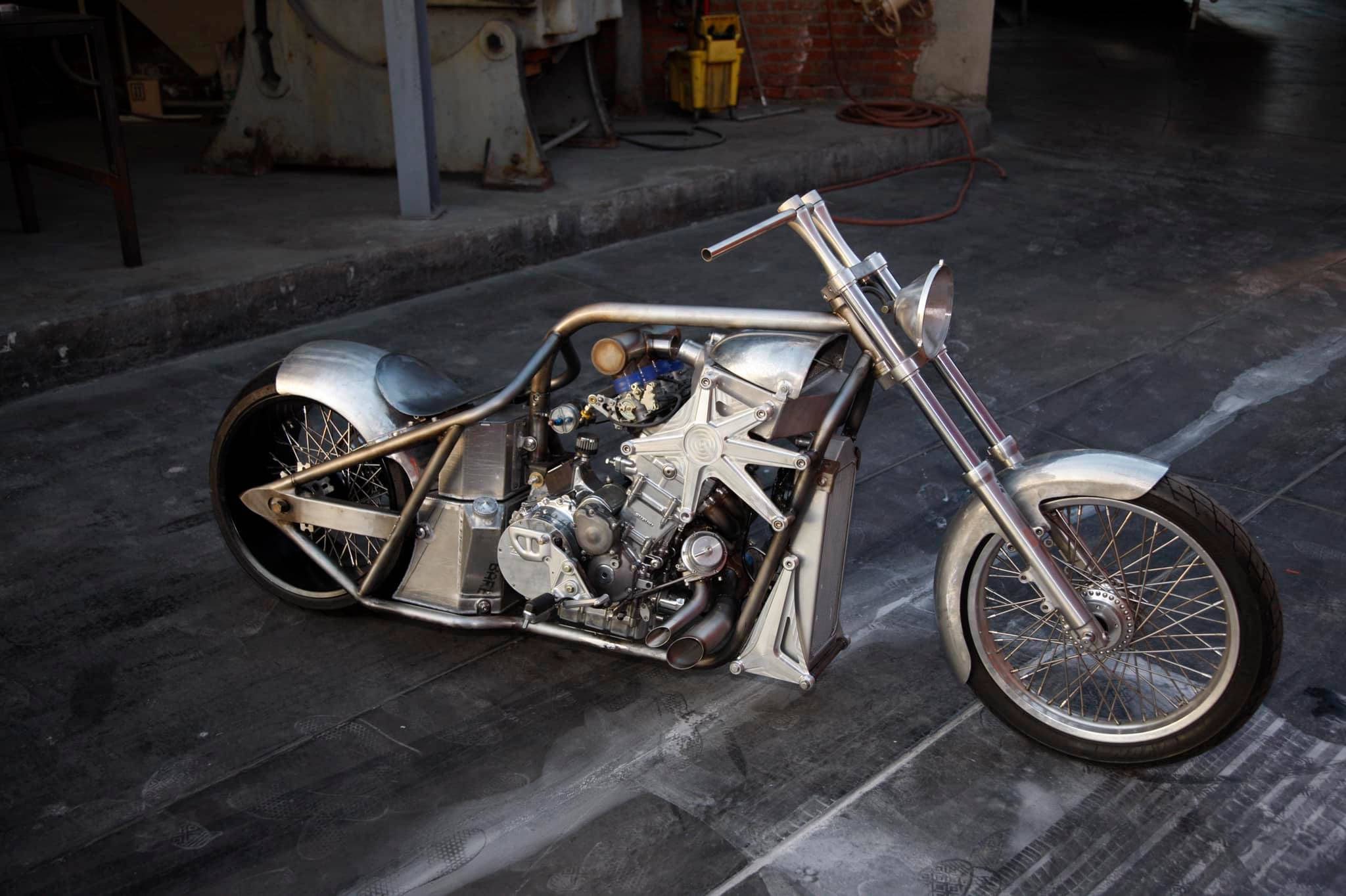 Choppers 桌布 壁紙 — 一架訂製的銀色chopper機車，帶有外露引擎和鍍鉻細節，停放在光線昏暗的車庫中潮濕的混凝土地板上。