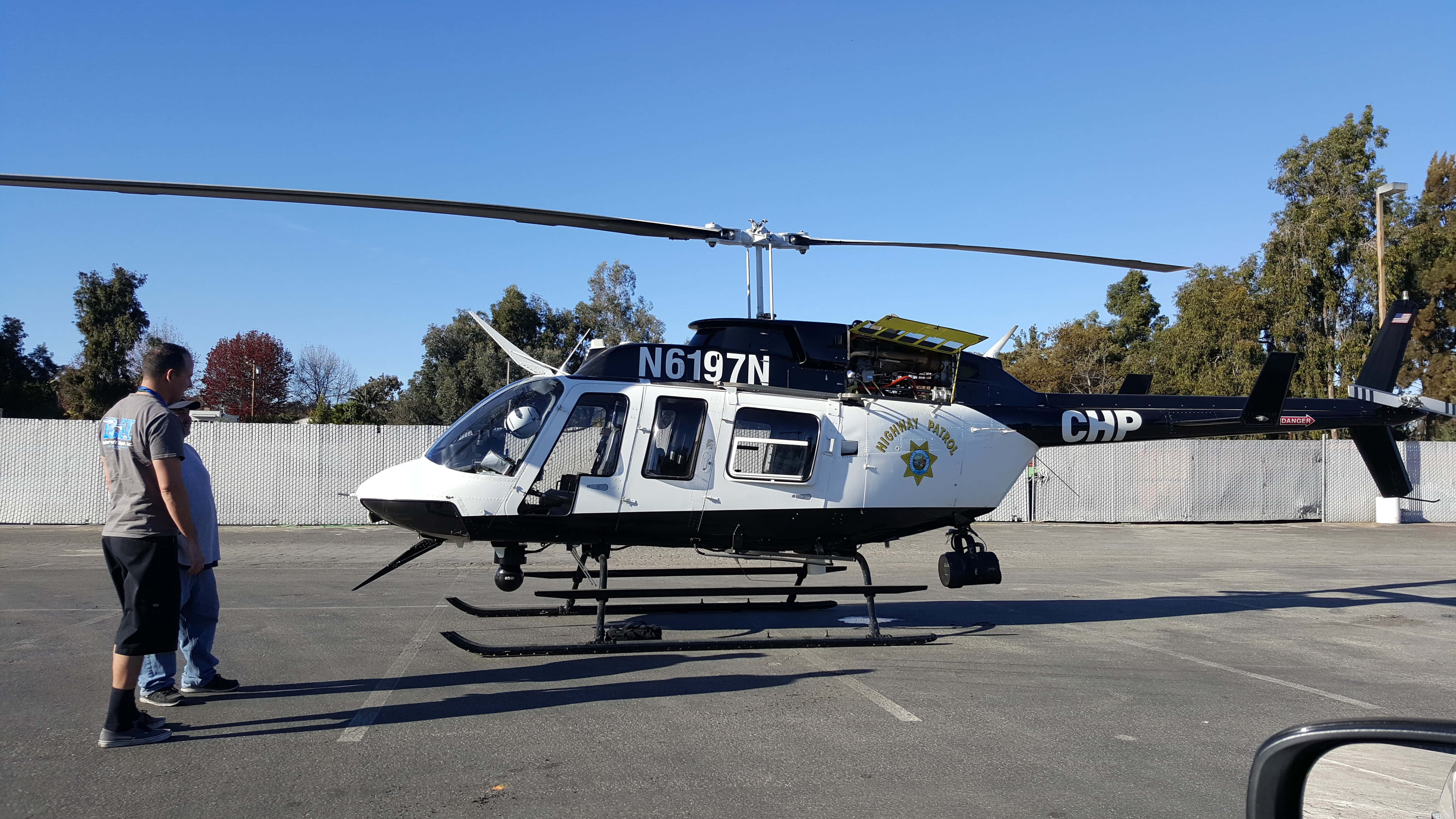 Helicopter 桌布 壁紙 — 一架註冊編號為N6197N的加州公路巡邏直升機停在瀝青地面上，天空清澈湛藍，兩名男子正在觀察它。