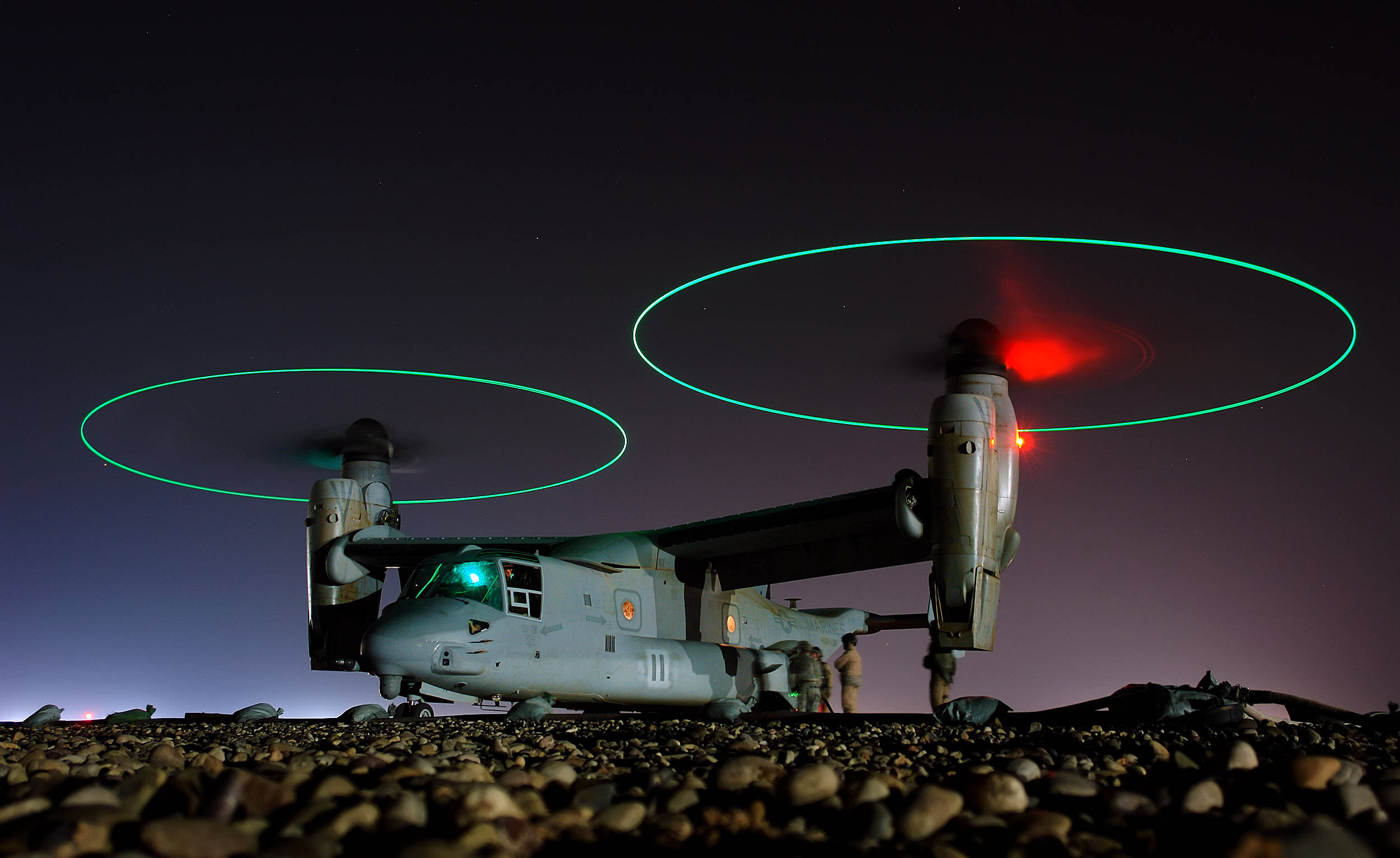 Military Helicopter 桌布 壁紙 — 一架軍用傾轉旋翼機在夜間懸停，發光的綠色旋轉翼軌跡和紅色導航燈映襯著星空。