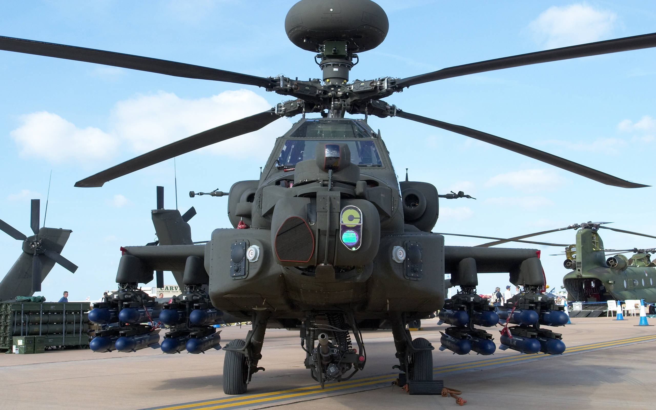 Helicopter 桌布 壁紙 — 一架軍用攻擊直升機，配備旋翼葉片和外置燃料箱，停放在停機坪上，背景是晴朗的藍天。