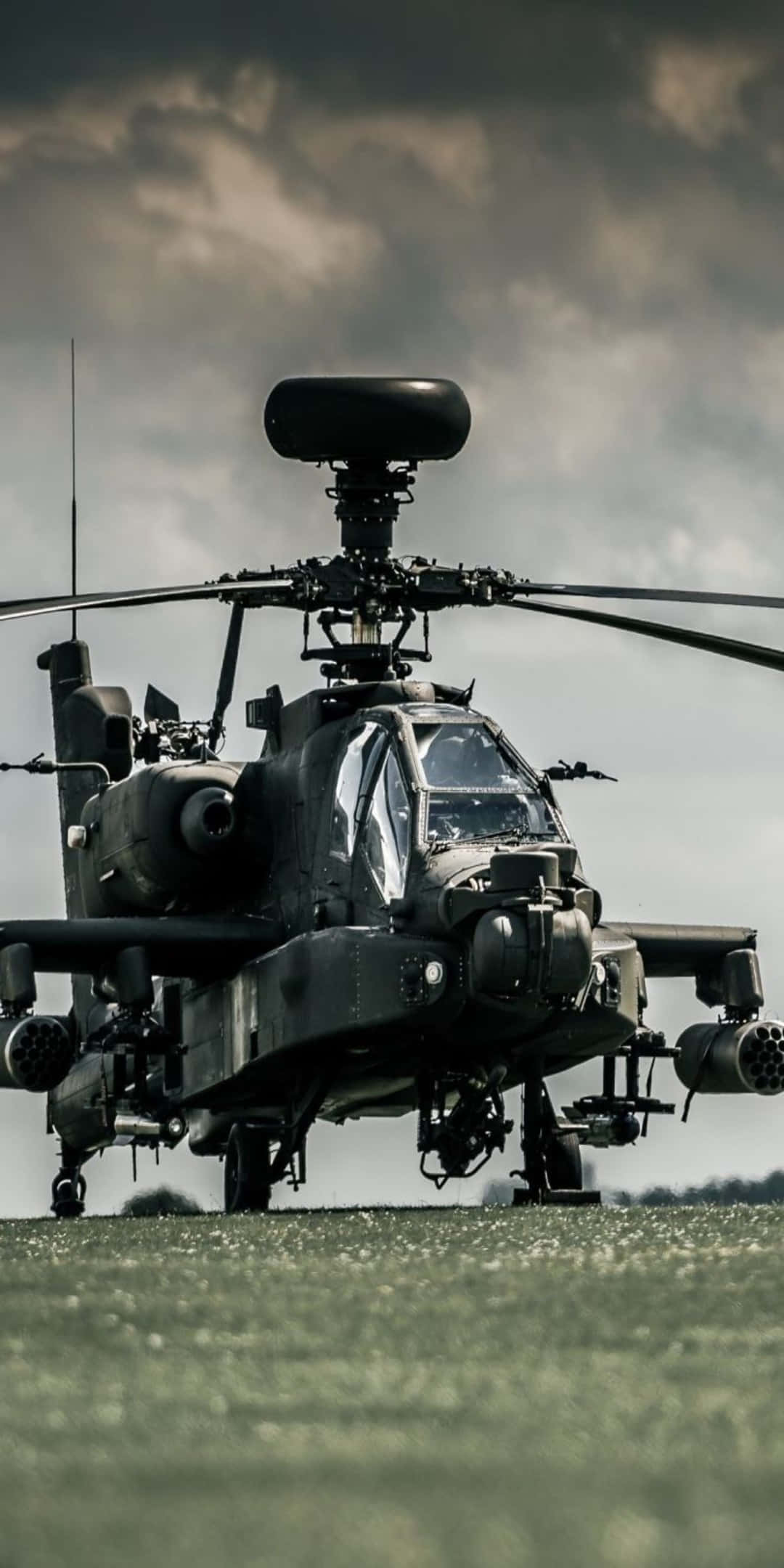 Helicopter 桌布 壁紙 — 一架軍用攻擊直升機在戲劇性的多雲天空下，佇立在草地上。