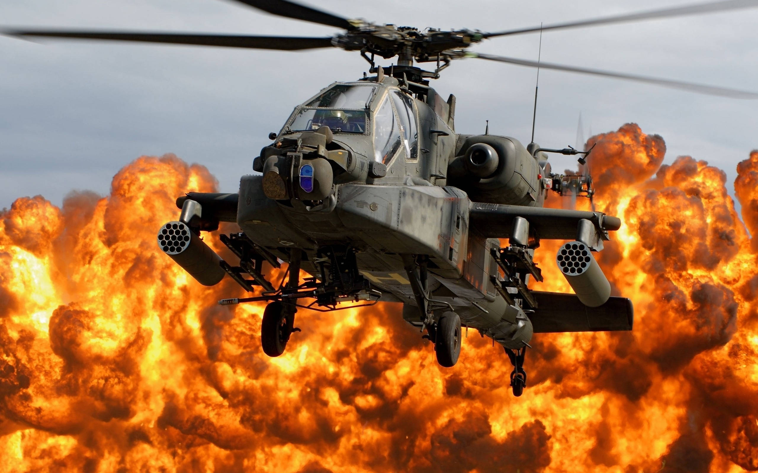 Helicopter 桌布 壁紙 — 一架軍用攻擊直升機在雲層天空背景下，旋轉著旋翼飛過熾熱的爆炸。