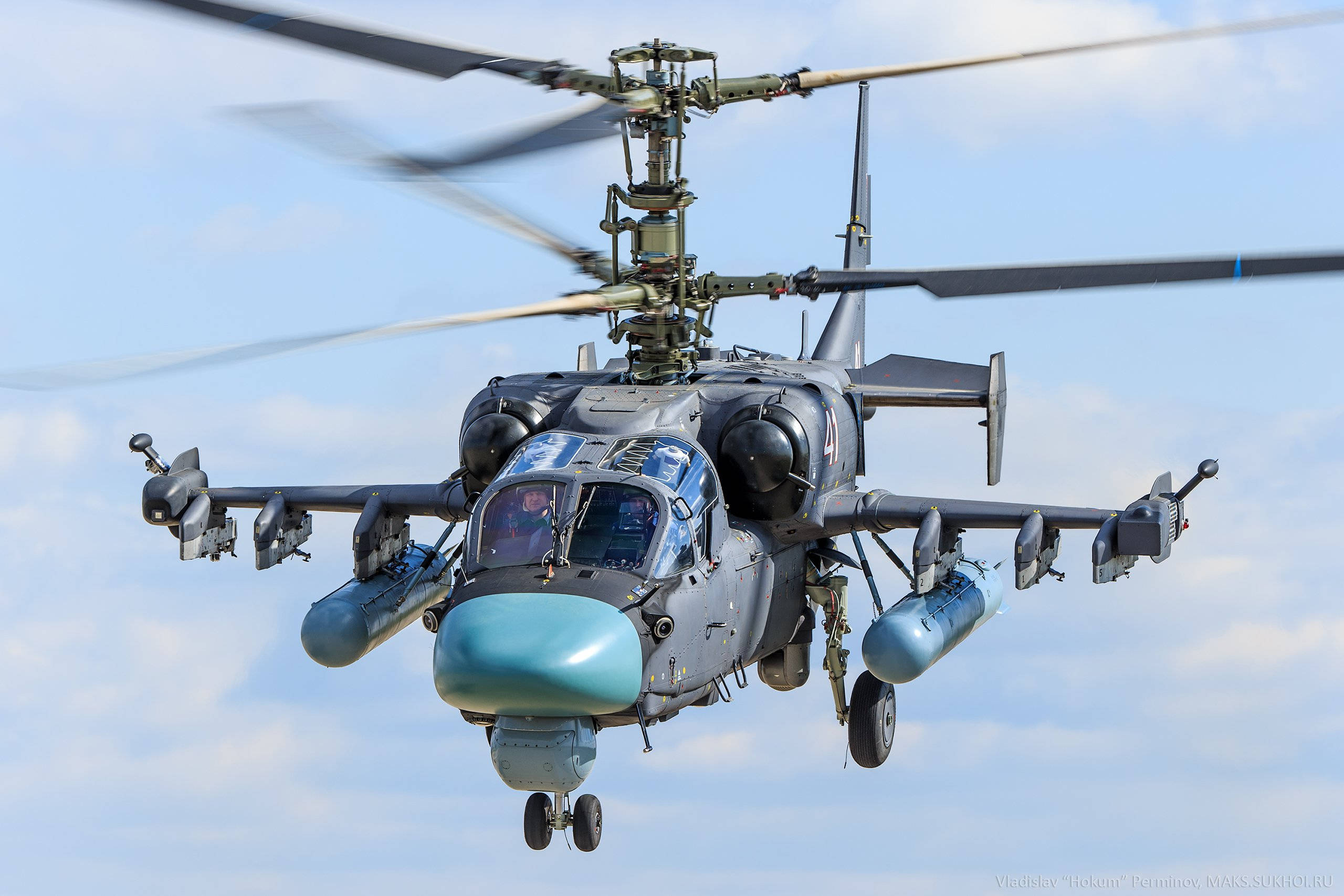 Helicopter 桌布 壁紙 — 一架軍用攻擊直升機帶有旋轉的旋翼和安裝的武器，在晴朗藍天和零星雲朵中低飛。