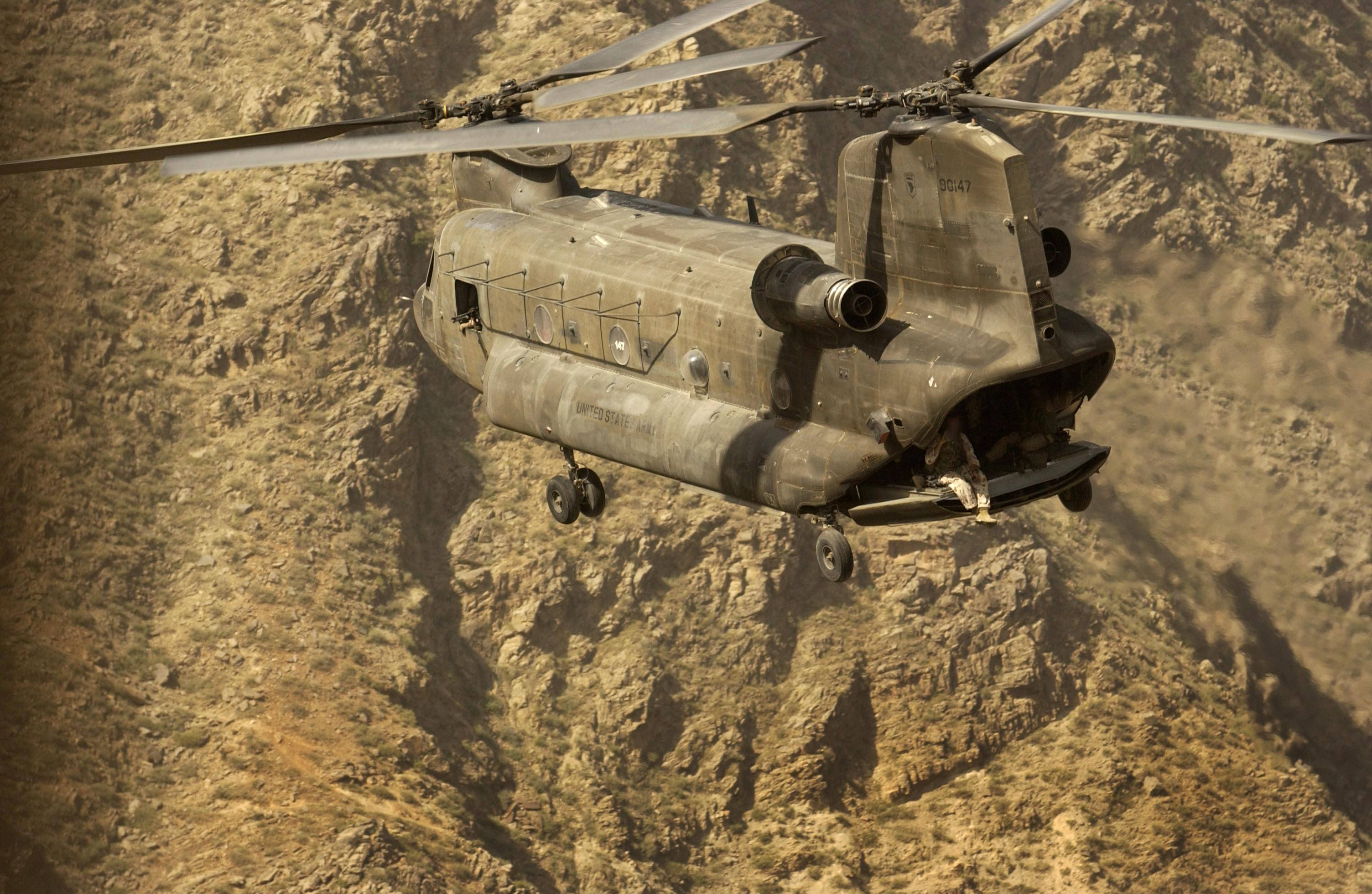 Helicopter 桌布 壁紙 — 一架軍用直升機低飛越過崎嶇的沙漠峽谷地形，揚起下方的灰塵。