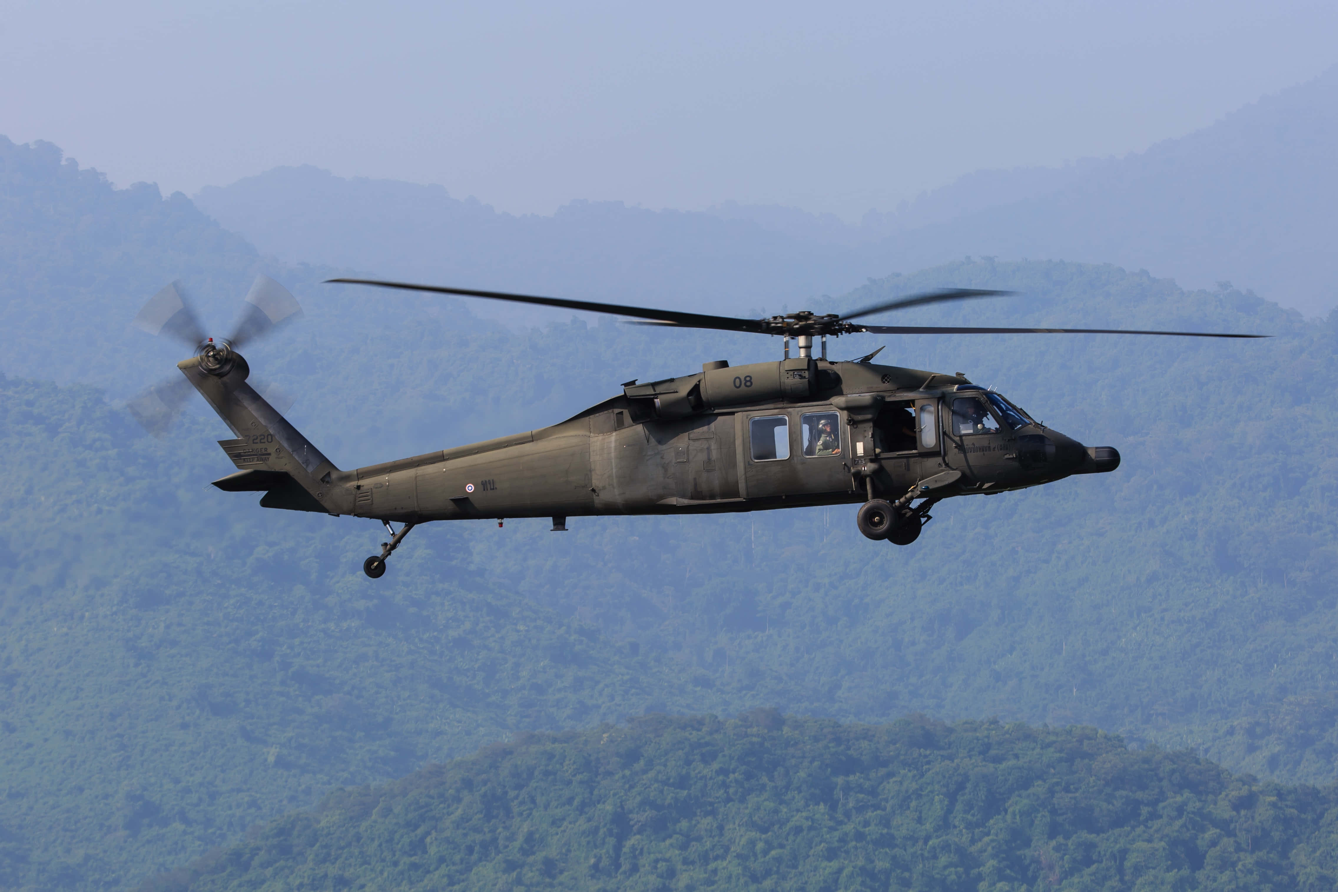 Helicopter 桌布 壁紙 — 一架軍用直升機低飛過茂密的綠色山脈，旋翼槳葉因運動而模糊。