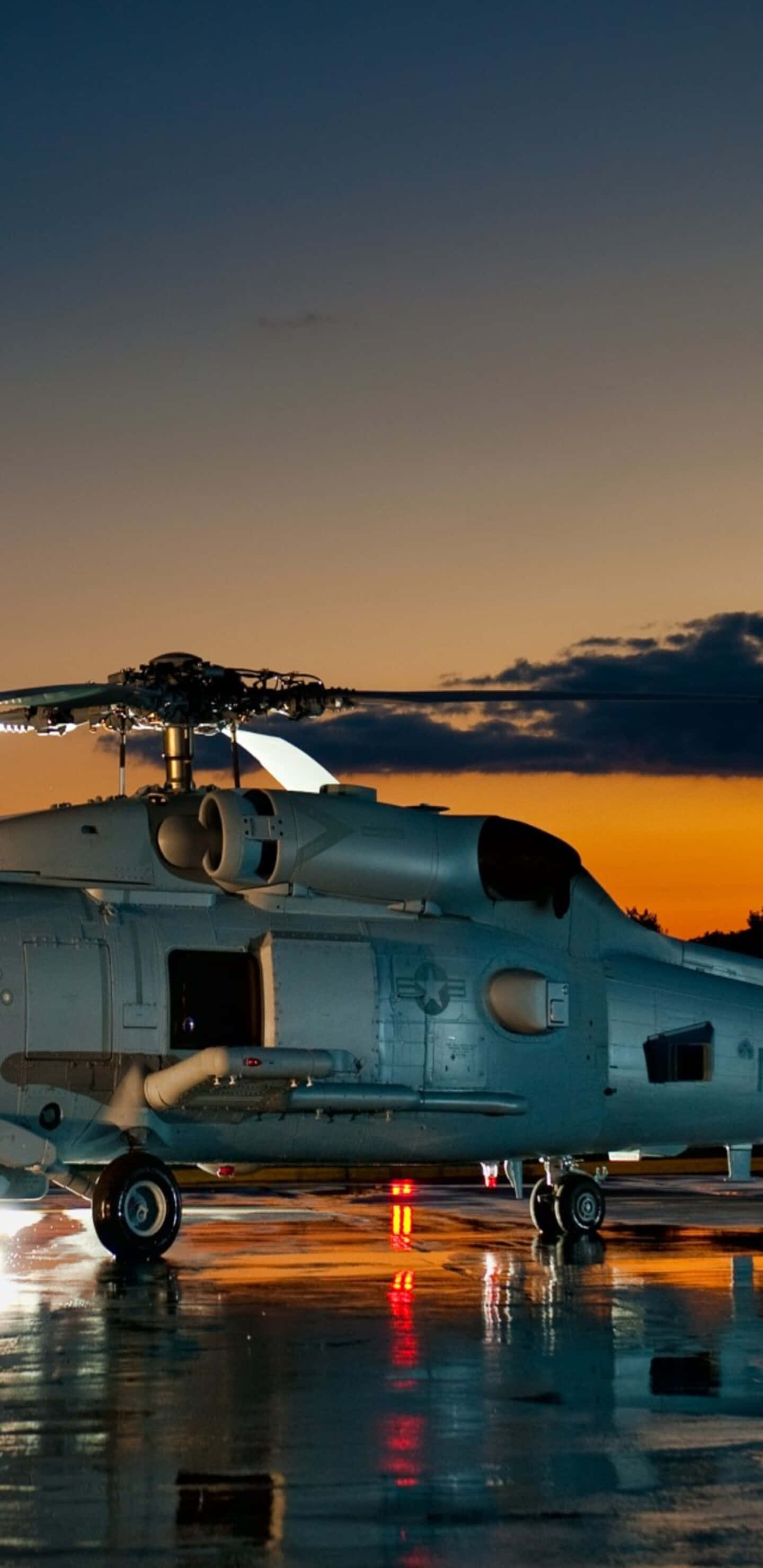 Helicopter 桌布 壁紙 — 一架軍用直升機停在濕滑的停機坪上，夕陽西下，鮮豔的橙色和藍色天空倒映在水坑中。