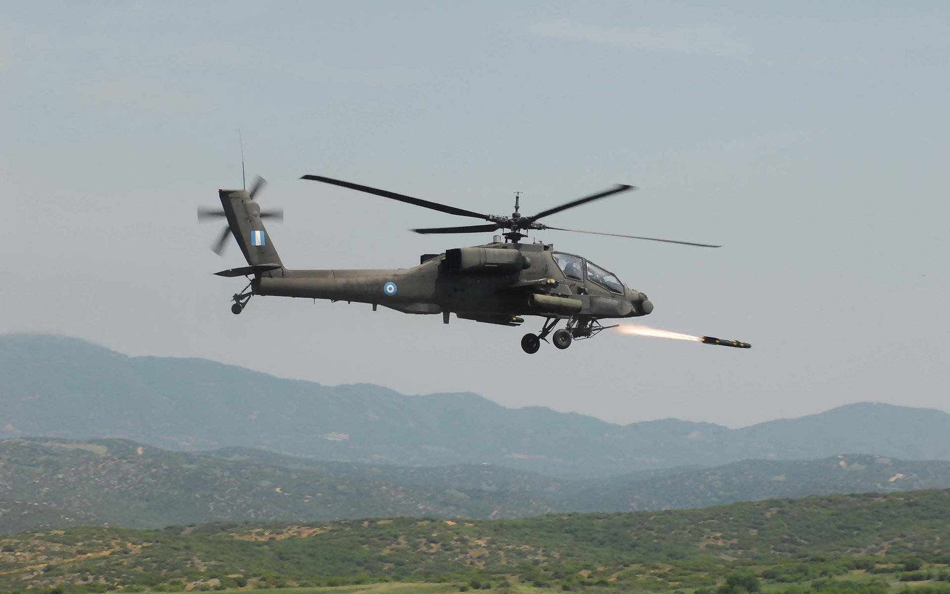Helicopter 桌布 壁紙 — 一架軍用直升機在朦朧的天空下向丘陵地帶發射導彈。