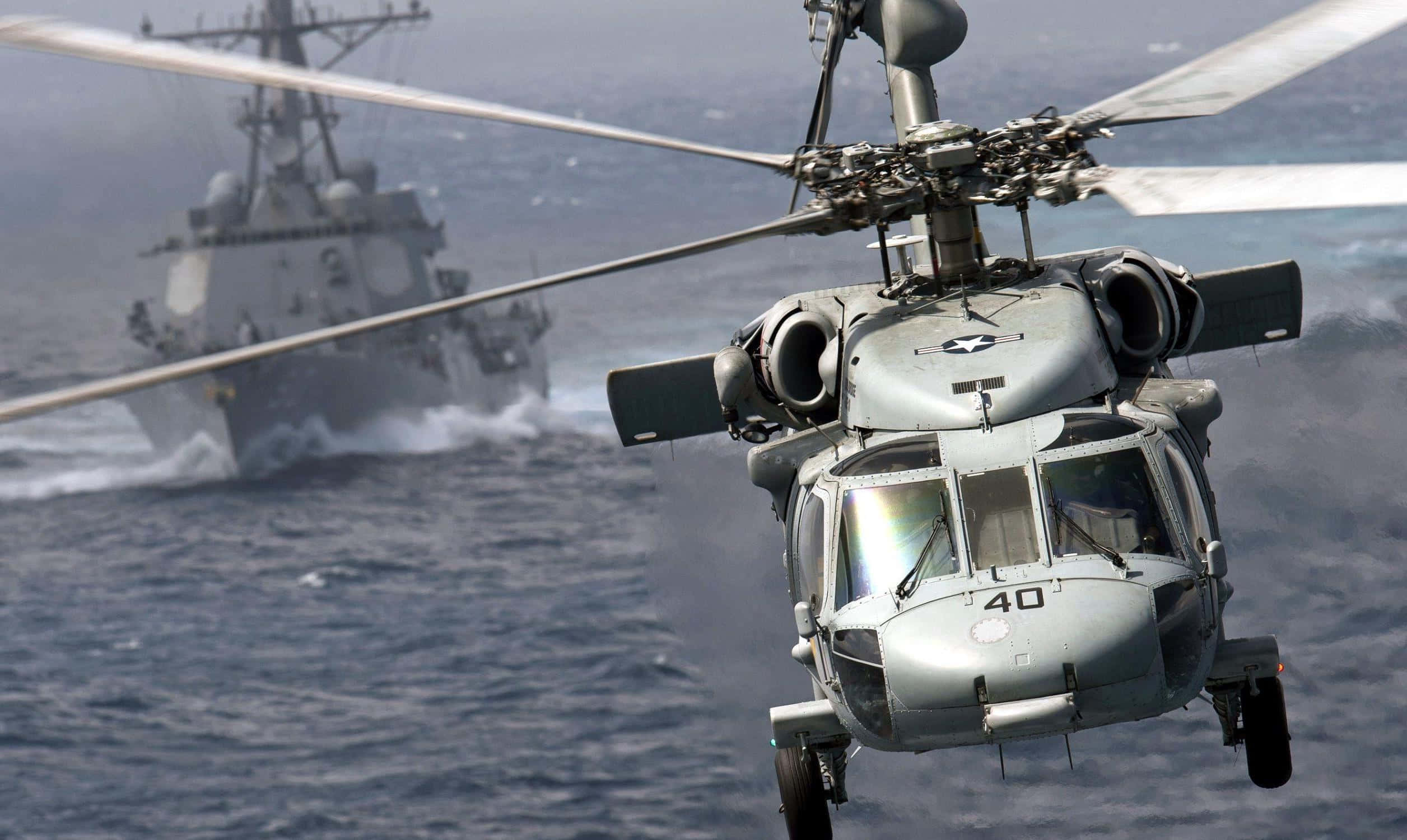 Helicopters 桌布 壁紙 — 一架軍用直升機在波濤洶湧的海面上盤旋，背景中一艘軍艦破浪前行。