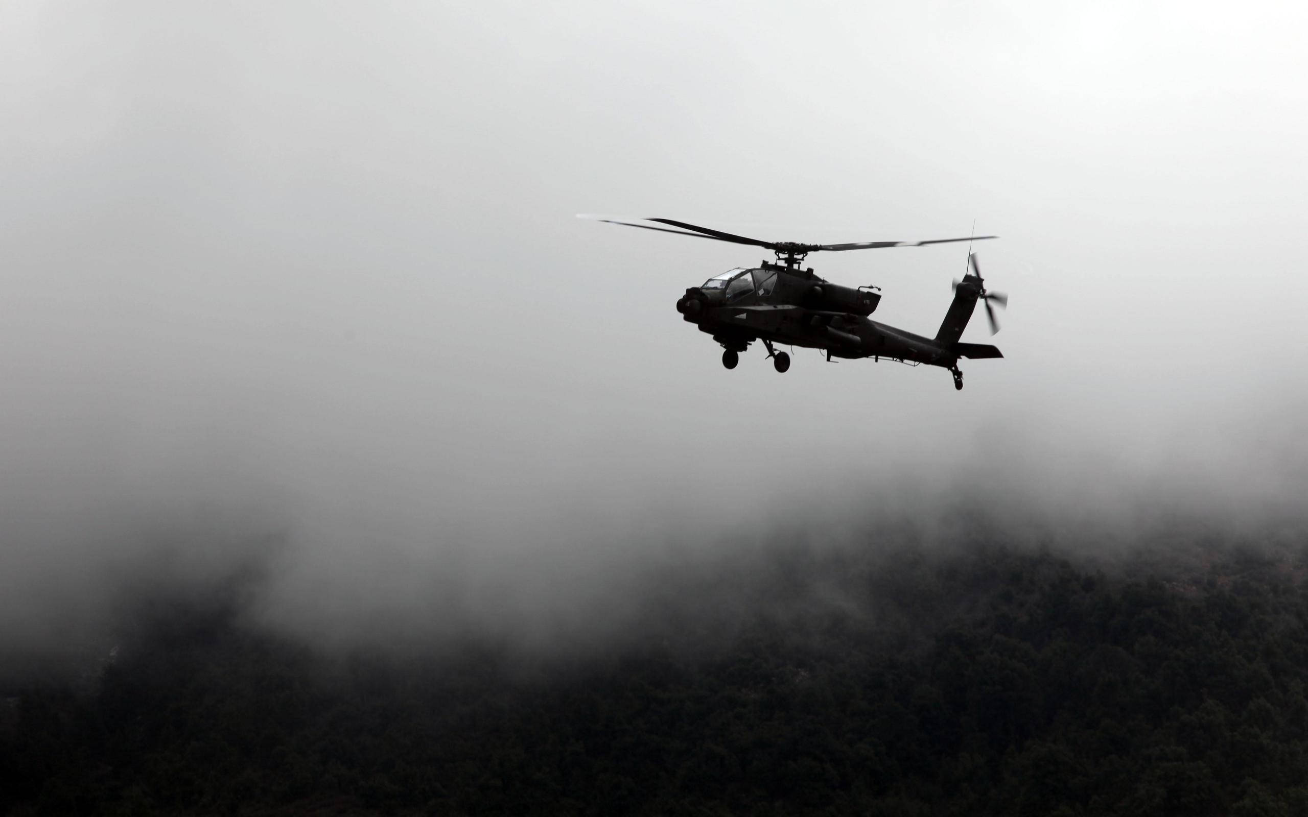 helicopter 4K 桌布 壁紙 — 一架軍用直升機在濃霧密佈的天空中呈現剪影，盤旋在森林覆蓋的山脈之上。
