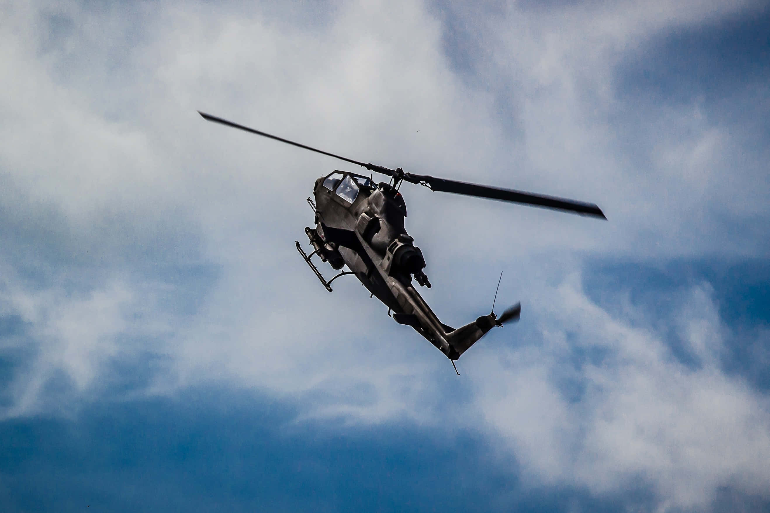 Helicopter 桌布 壁紙 — 一架軍用直升機在藍白雲朵的動態天空中翱翔，旋翼轉動。
