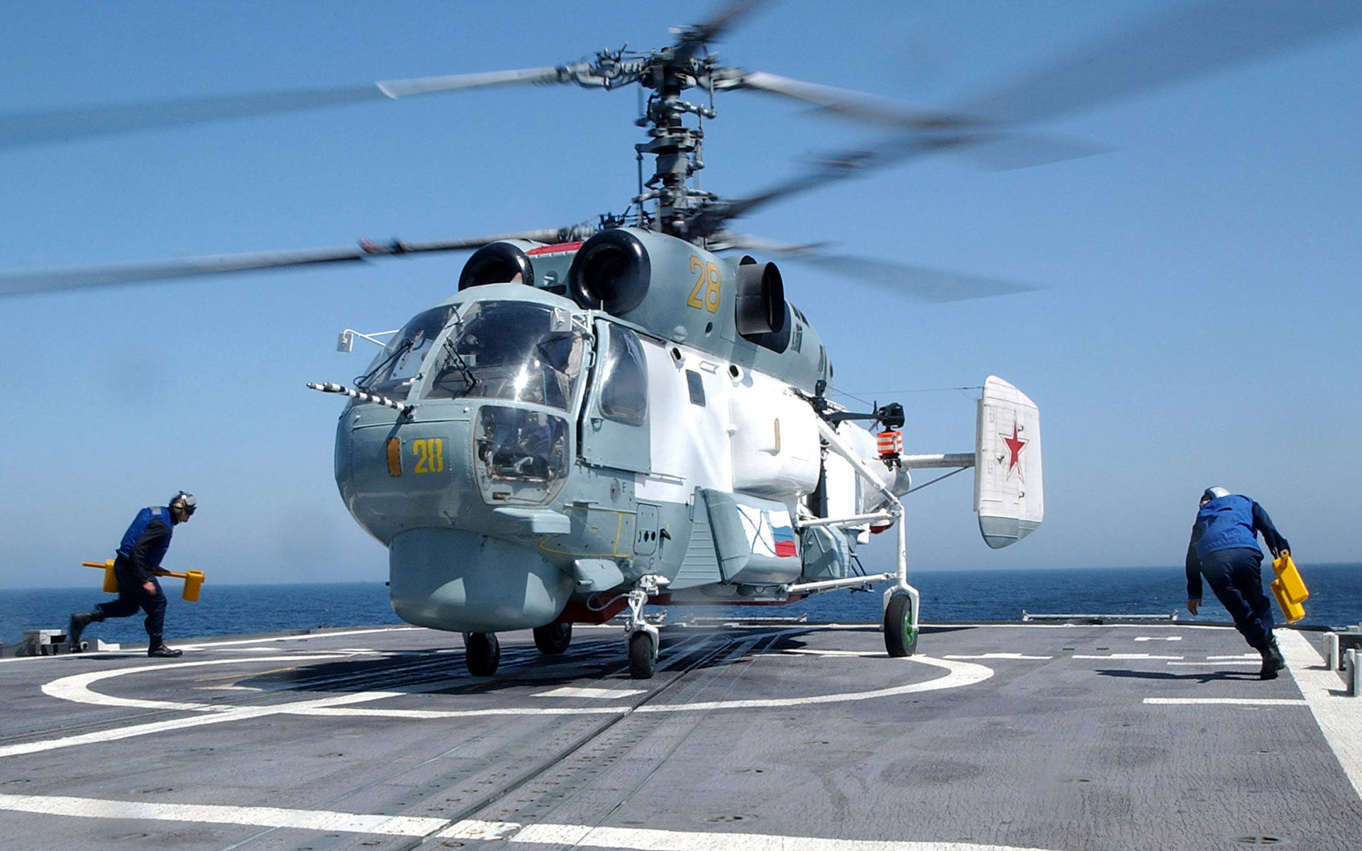 Helicopter 桌布 壁紙 — 一架軍用直升機旋轉著槳葉停在航空母艦甲板上，機組人員在清澈的藍天下引導它。