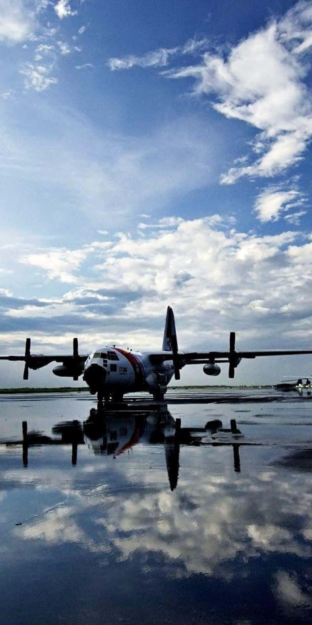 Pixel 3 Plane 桌布 壁紙 — 一架軍用運輸機停在潮濕的停機坪上，倒映出晴朗的藍天和蓬鬆的白雲。