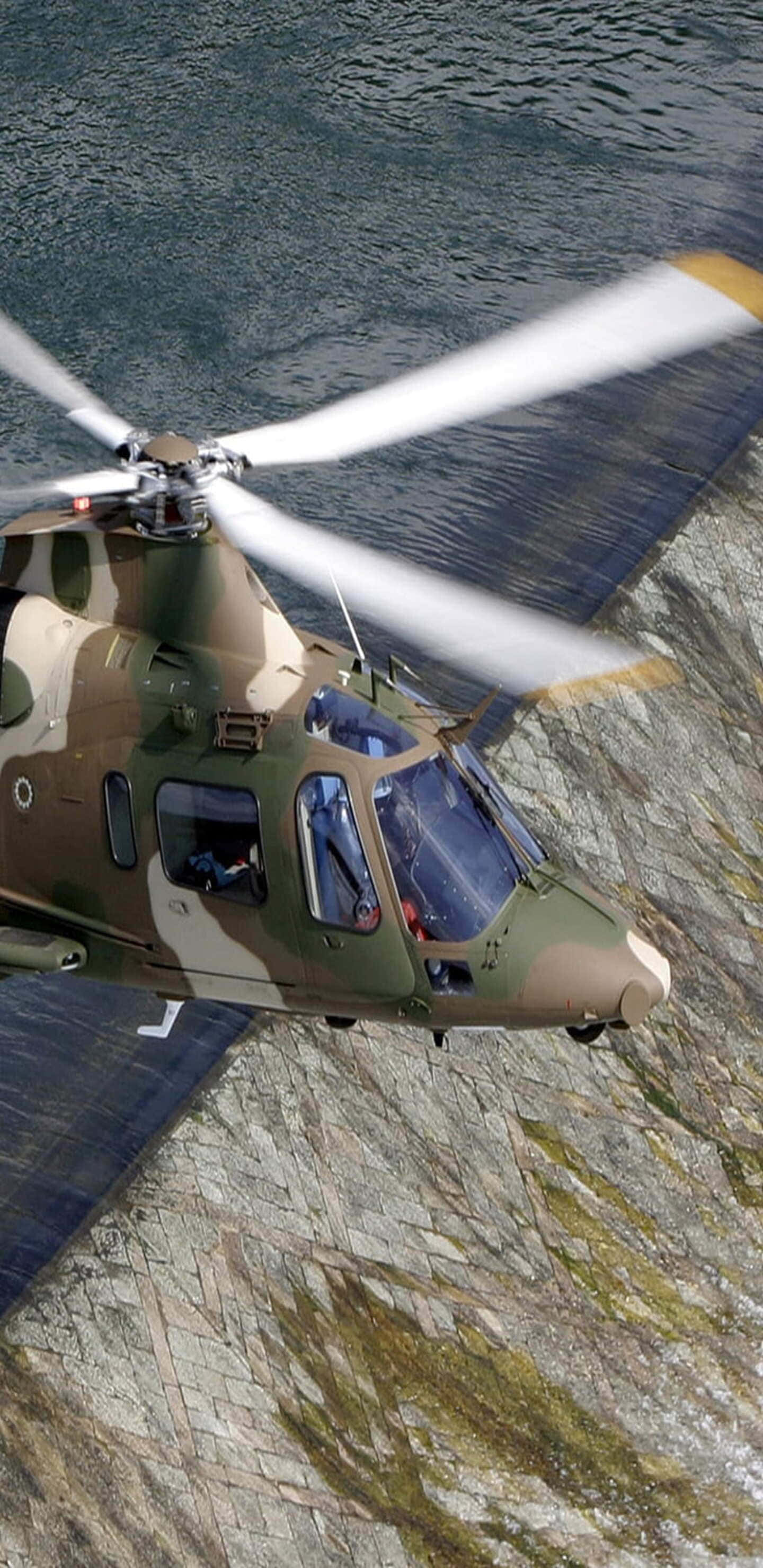 Helicopter 桌布 壁紙 — 一架迷彩軍用直升機低飛過岩石峭壁，旋翼葉片模糊。