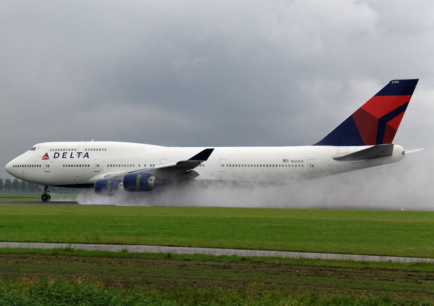 飛機 桌布 壁紙 — 一架達美波音747在多雲的天空下於潮濕的跑道上降落，濺起水花。