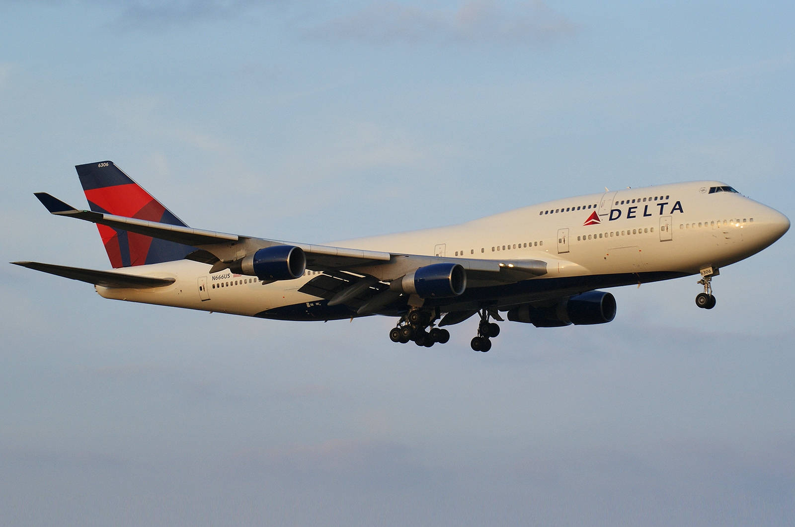 flying 桌布 壁紙 — 一架達美航空波音747飛機正在降落，起落架放下，背景是柔和藍天和零星雲朵。