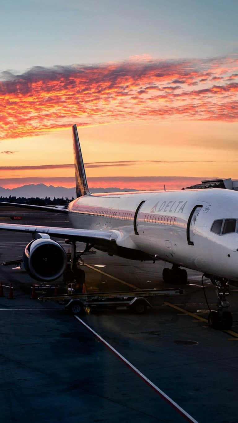 Plane 桌布 壁紙 — 一架達美航空飛機停在停機坪上，火紅的橙色和粉紅色雲彩在遠山之上的暮色天空中蔓延。