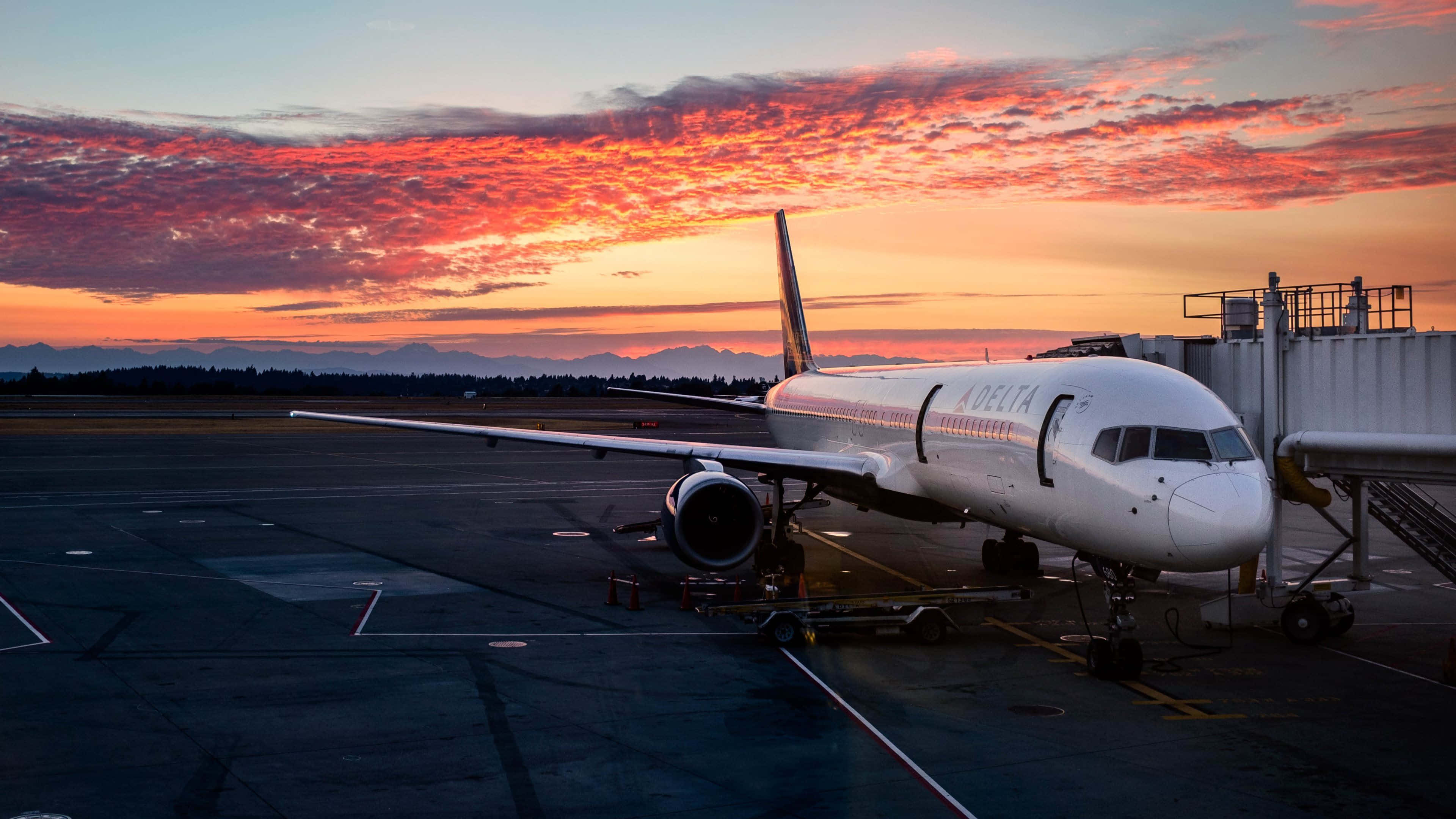 桌布 壁紙 — 一架達美航空飛機停在機場閘口，天空是火燒般的夕陽，有橙粉色的雲彩。
