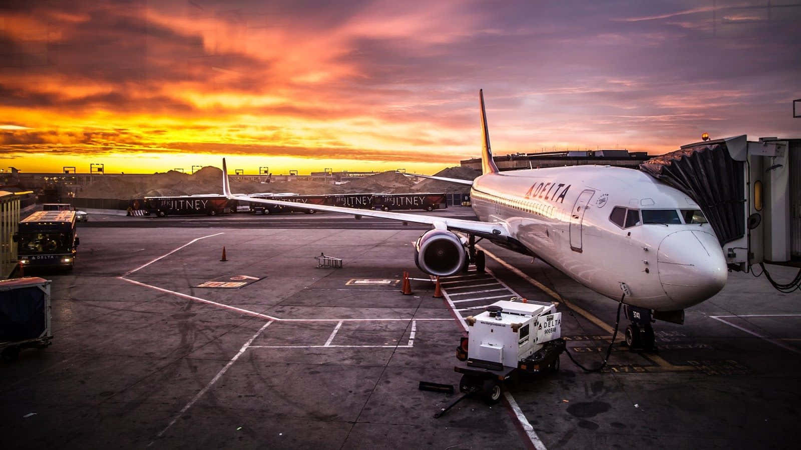 飛機 桌布 壁紙 — 一架達美航空飛機停在機場閘口，背景是火紅橙紫的日落天空。