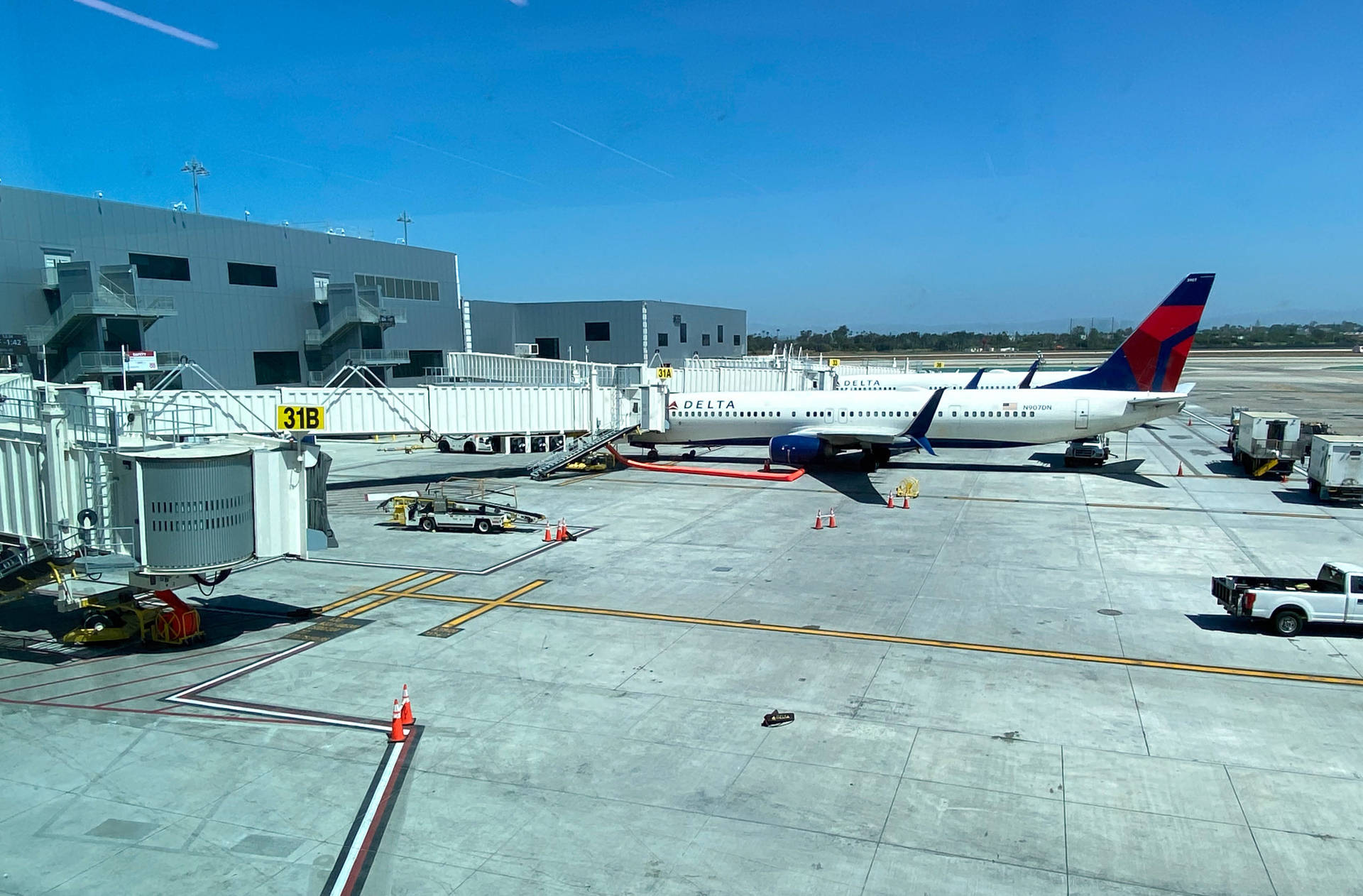 飛機 桌布 壁紙 — 一架達美航空飛機停泊在31B登機門，晴空萬里，機場地面設備和空橋清晰可見。