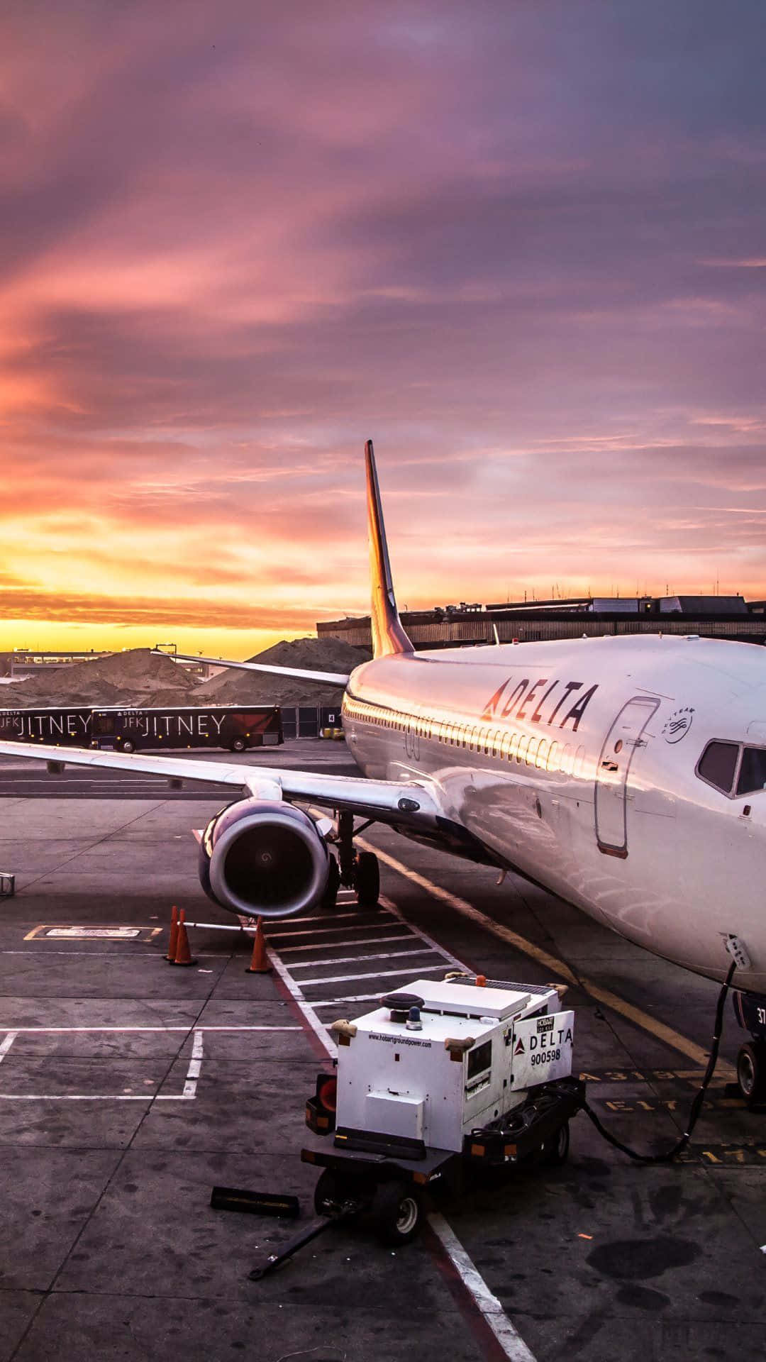 Plane 桌布 壁紙 — 一架達美航空飛機在日落時停放在機場停機坪上，上方有鮮豔的粉紅色和橙色雲彩。