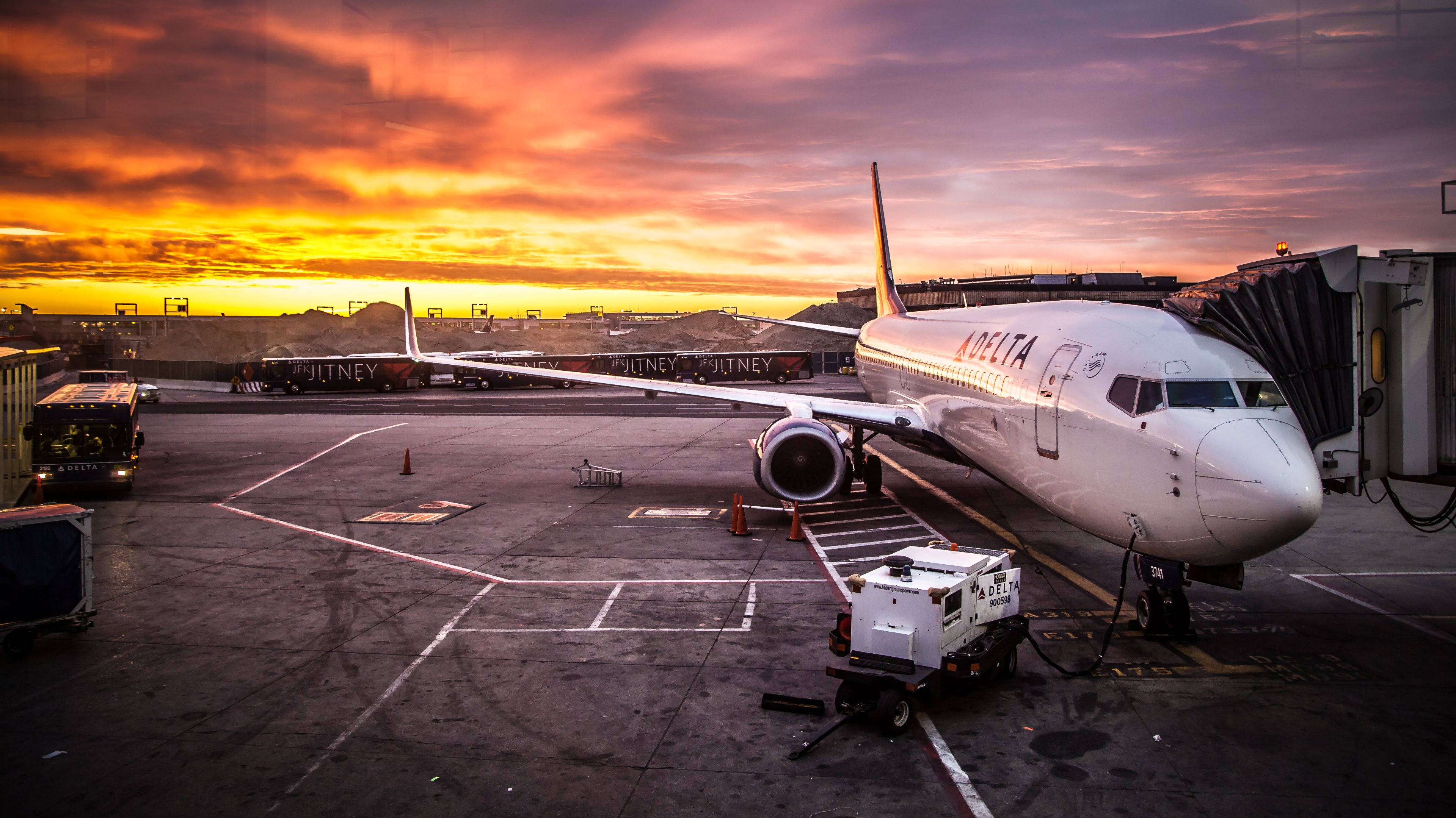 Plane 桌布 壁紙 — 一架達美航空飛機在火紅橙紫的日落時分停泊在機場閘口。
