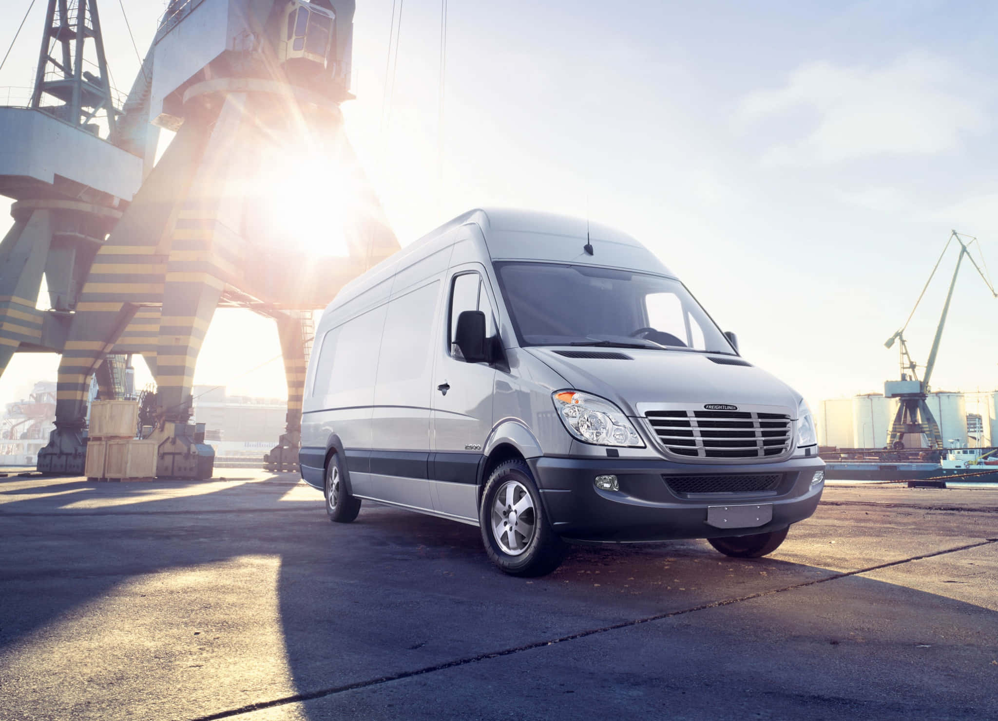 Van 桌布 壁紙 — 一架銀色 Mercedes-Benz Sprinter 客貨車停放在陽光普照的工業港口，大型起重機投下長長的陰影。