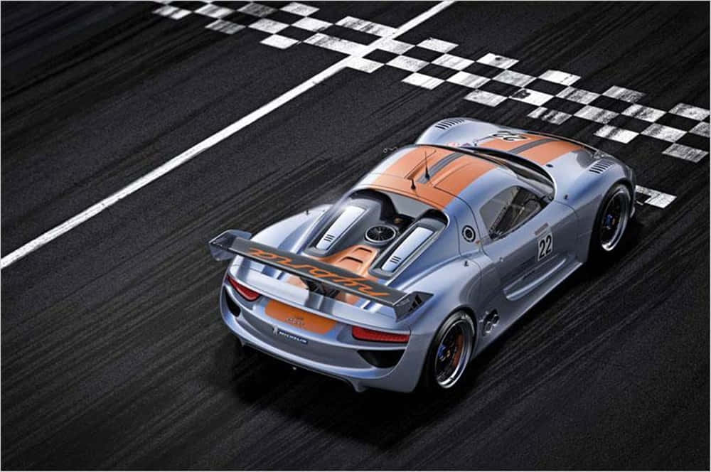 Car Racing 桌布 壁紙 — 一架銀色和橙色的保時捷賽車從高角度俯瞰，在黑暗的賽道上越過方格旗終點線。