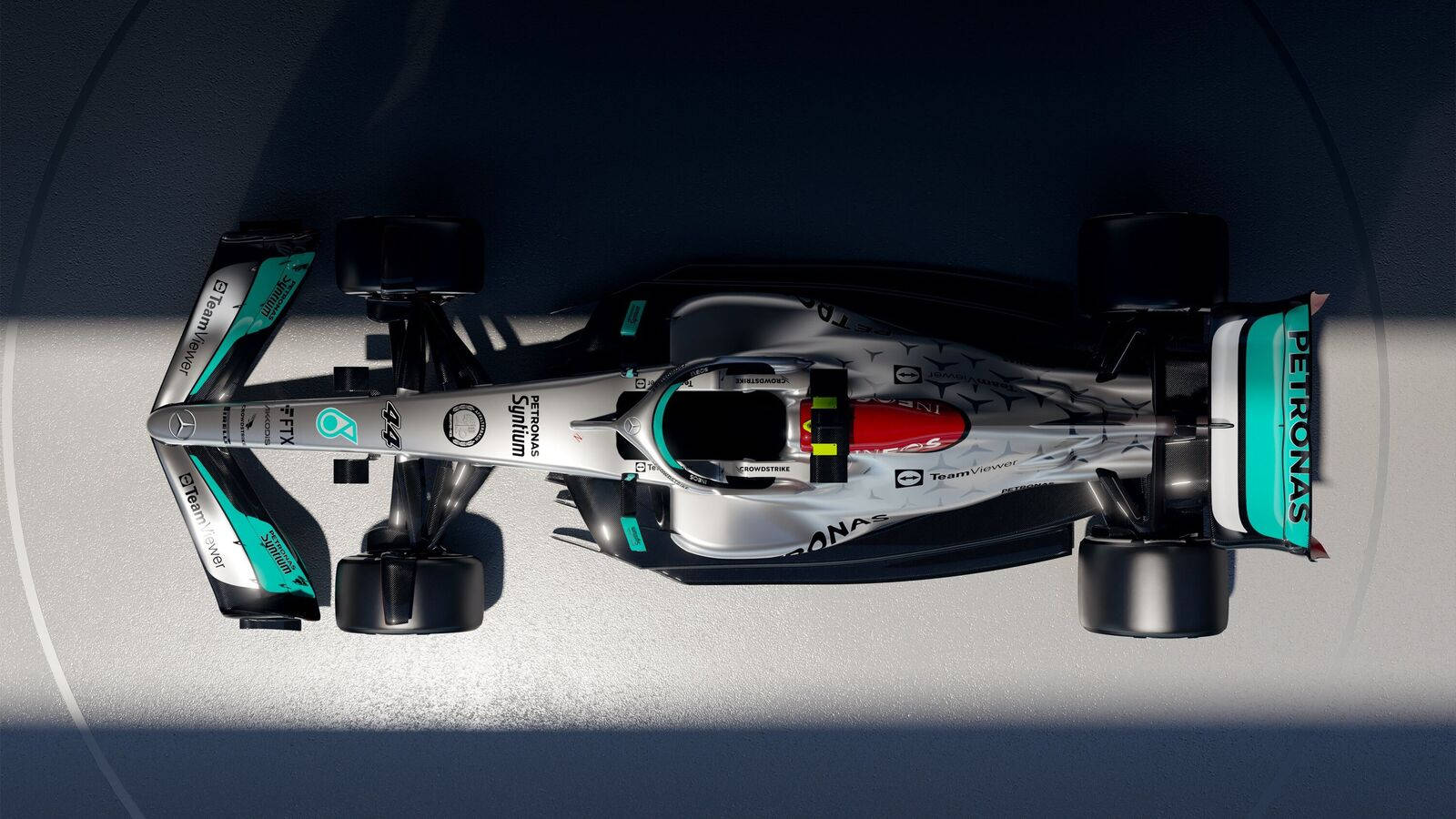Mercedes 桌布 壁紙 — 一架銀色和藍綠色的 Formula 1 賽車帶有 Petronas 品牌標誌，在戲劇性燈光下停放在混凝土表面上的鳥瞰圖。