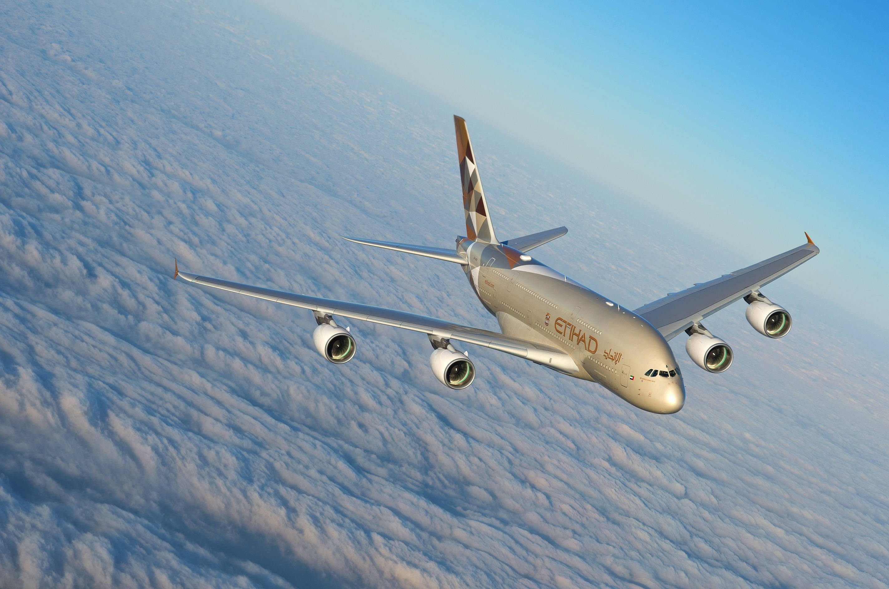 flying 桌布 壁紙 — 一架銀色的阿提哈德航空空中巴士A380在晴朗的藍天下，優雅地翱翔在廣闊的蓬鬆白雲之上。