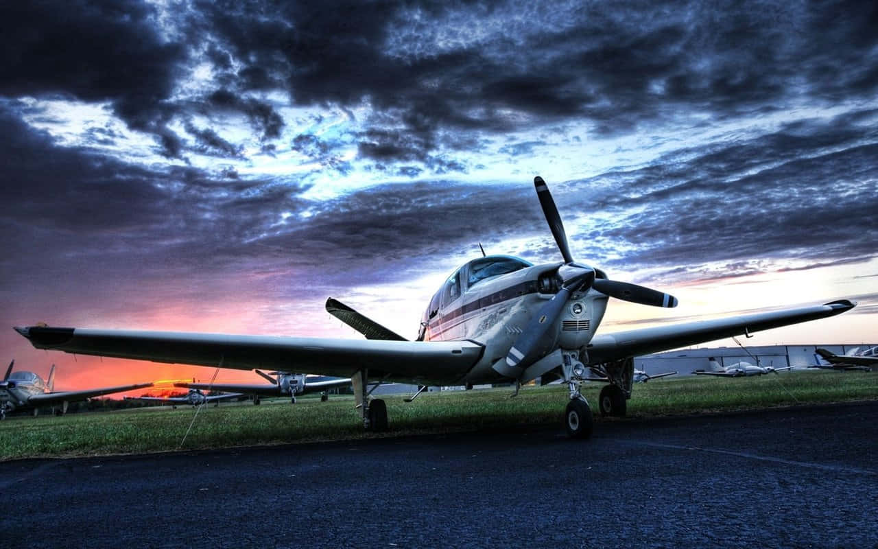 Aircraft 桌布 壁紙 — 一架銀色螺旋槳飛機停在停機坪上，背景是帶有紫色和橙色雲彩的戲劇性黃昏天空。
