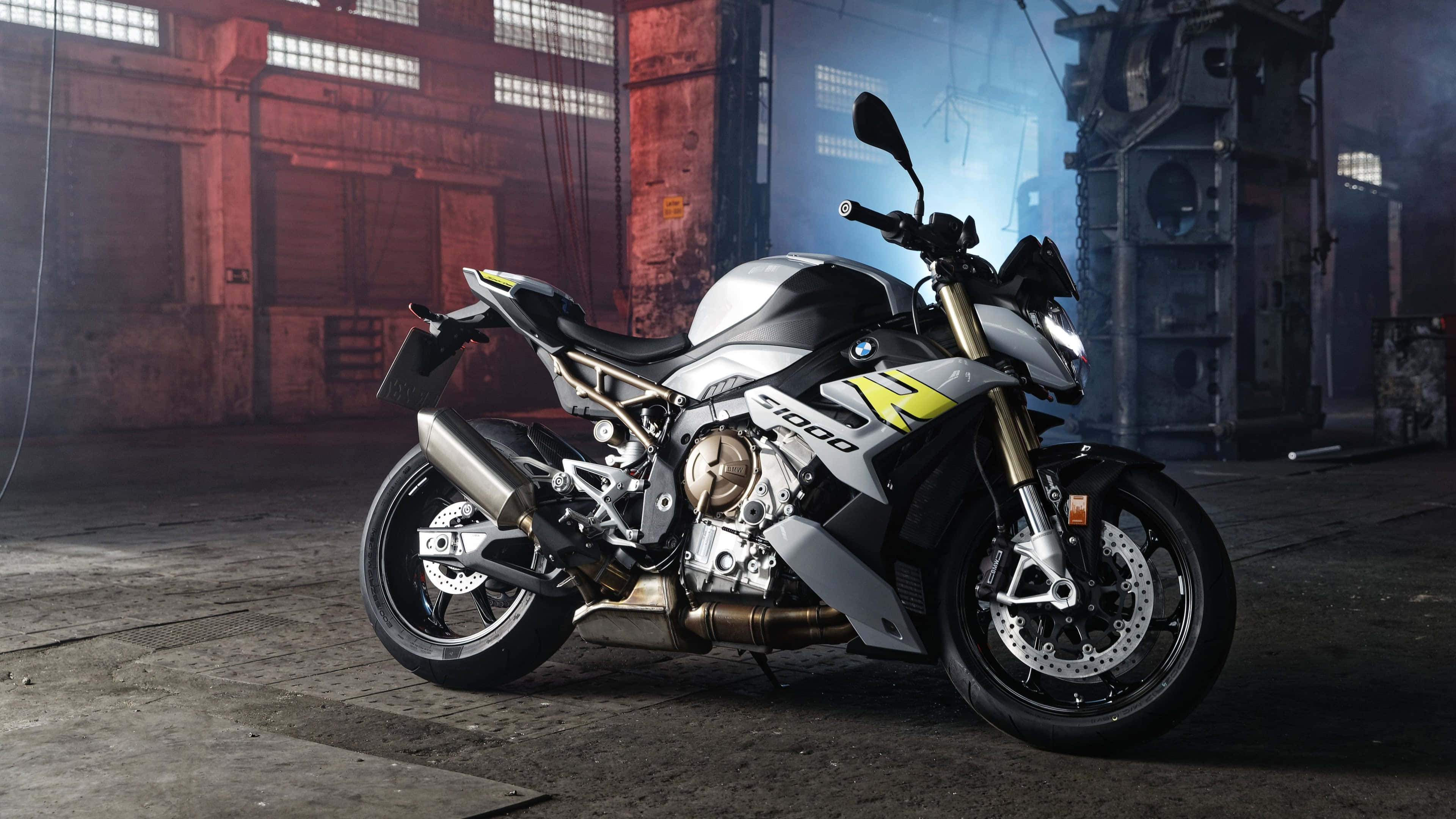4K Bikes 桌布 壁紙 — 一架銀黃色BMW S 1000 R摩托車，時尚地停放在燈光昏暗、有紅磚牆和鋼樑的工業倉庫中。