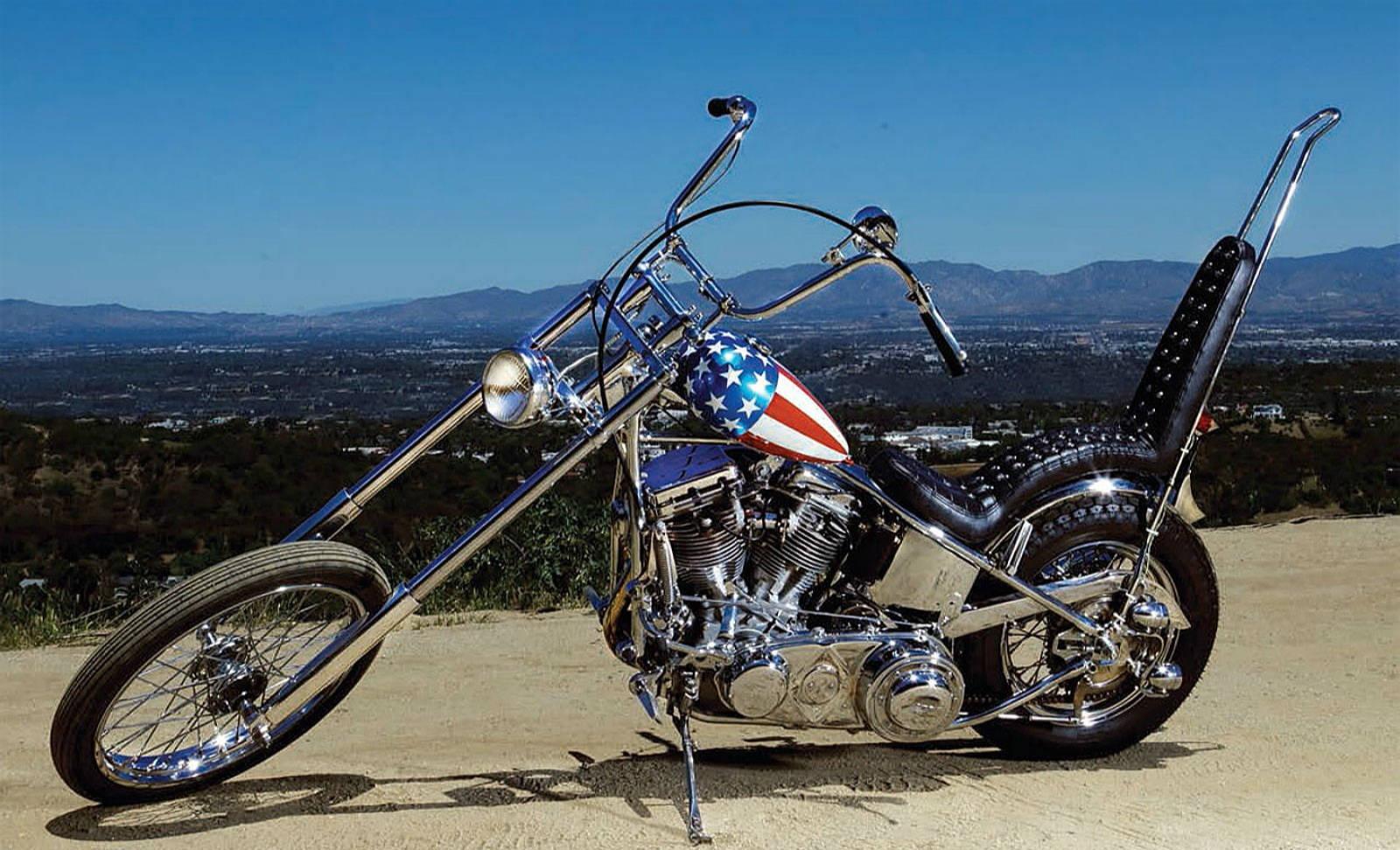Bobber 桌布 壁紙 — 一架鍍鉻chopper機車，帶有美國國旗油箱，矗立在小山上，俯瞰著晴朗藍天下廣闊的山谷。