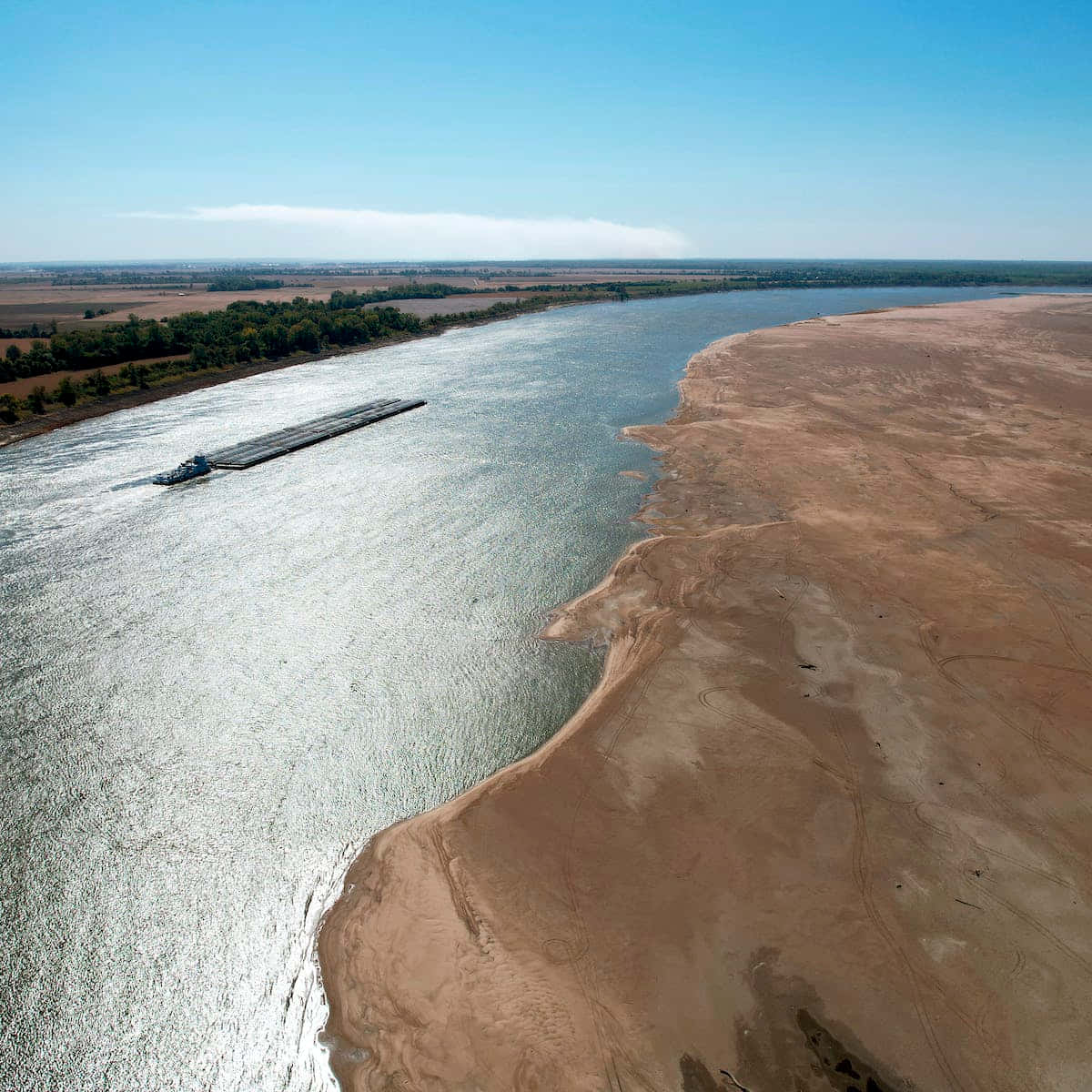 river 桌布 壁紙 — 一架長長的駁船在寬闊的河流中航行，旁邊是廣闊的裸露沙洲，天空清澈湛藍的航拍視圖。