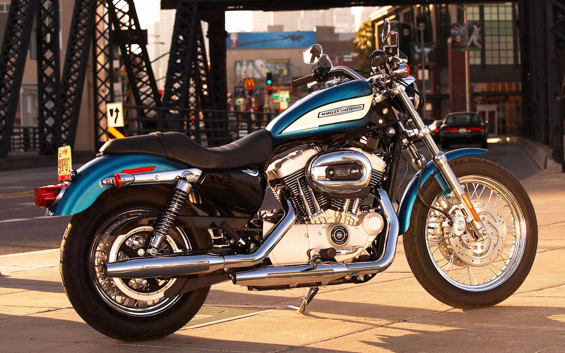 Harley 桌布 壁紙 — 一架閃亮的青綠色Harley-Davidson機車停在鋼橋下的陽光城市人行道上。