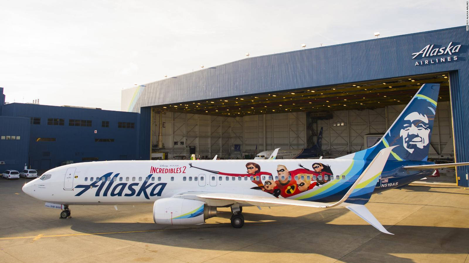 Plane 桌布 壁紙 — 一架阿拉斯加航空的波音737，機身印有超人特攻隊2角色，在明亮的日光下停放在機庫外。