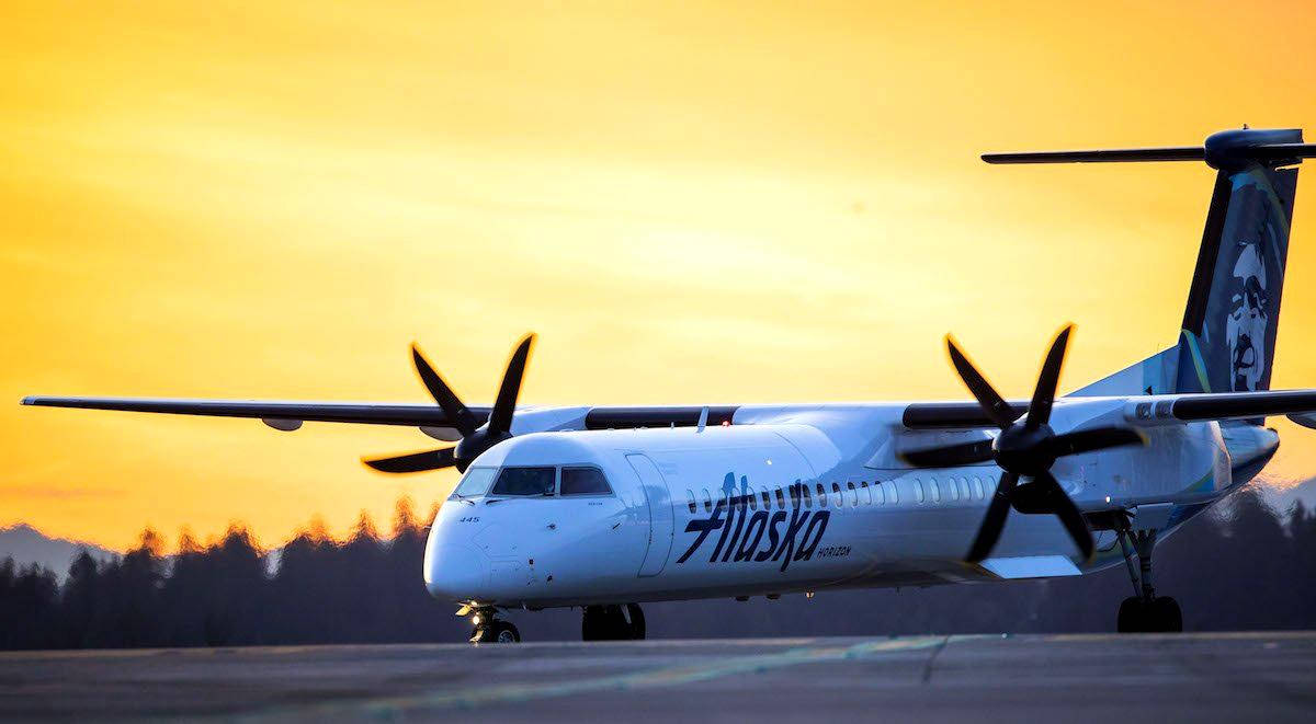 alaska 桌布 壁紙 — 一架阿拉斯加航空的渦輪螺旋槳飛機停在跑道上，沐浴在金色的夕陽中，遠處的樹木形成剪影。