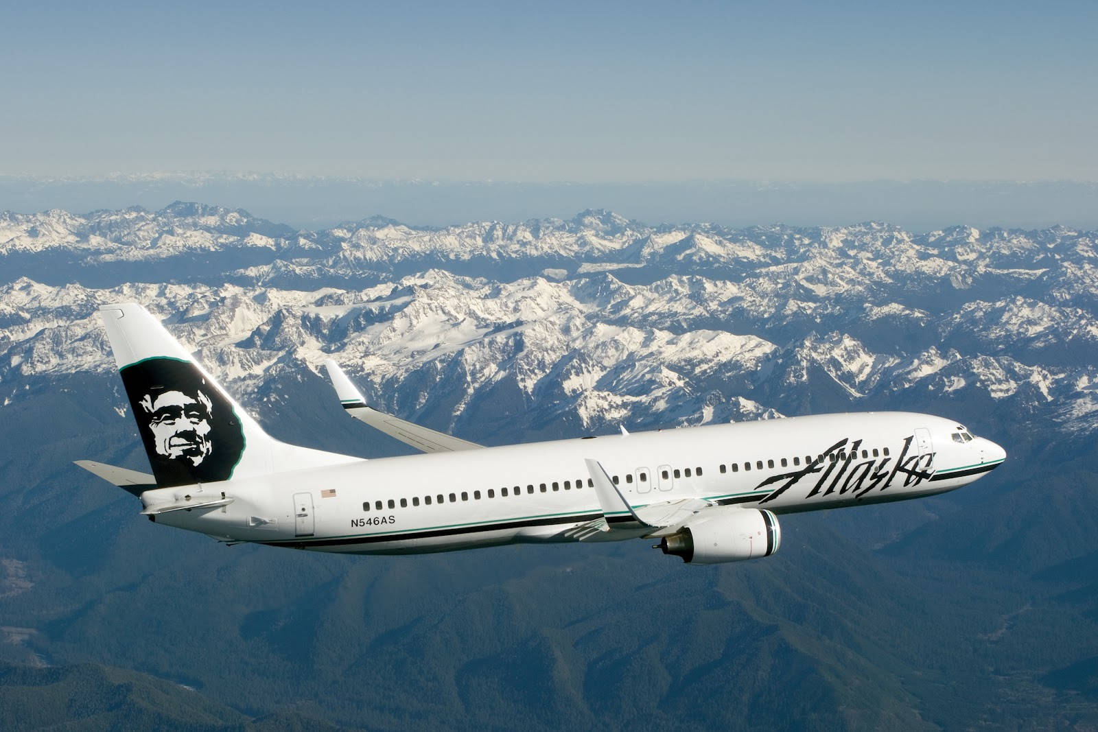 alaska 桌布 壁紙 — 一架阿拉斯加航空的飛機在晴朗的藍天下翱翔於積雪覆蓋的山脈之上。