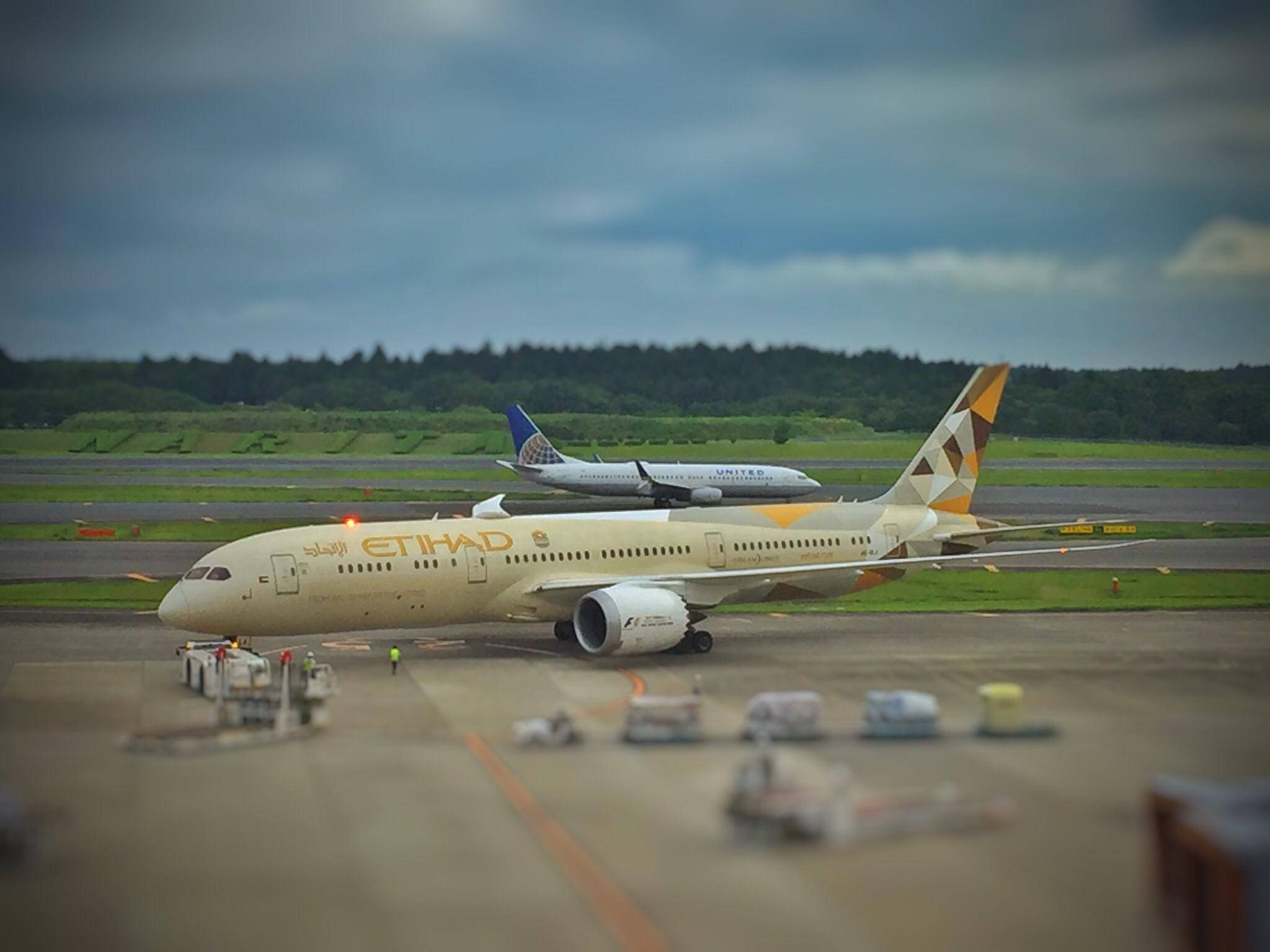 Aviation 桌布 壁紙 — 一架阿提哈德航空的飛機在潮濕的跑道上滑行，天空多雲，背景中可見另一架飛機。