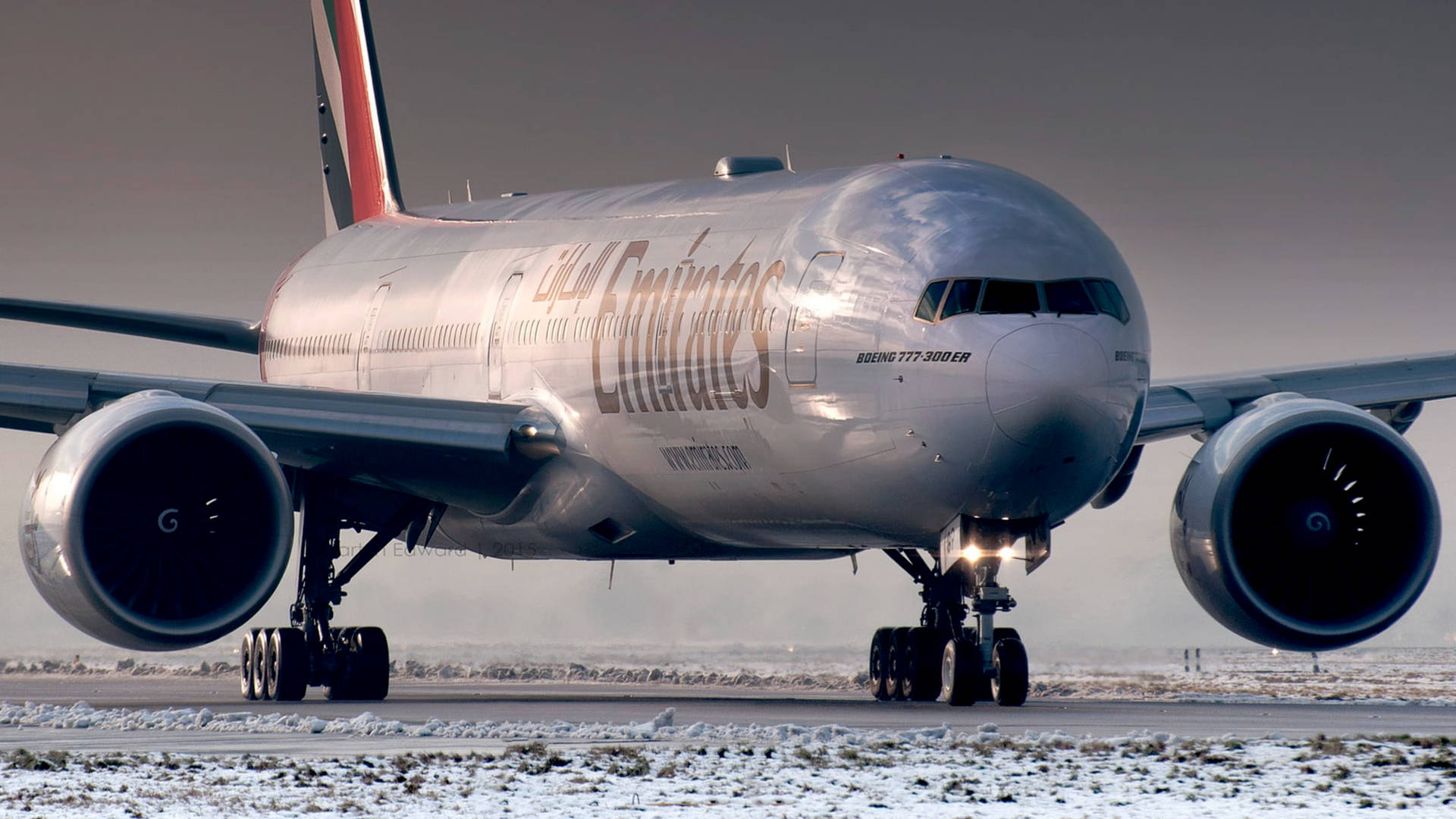  壁紙 — 一架阿聯酋航空波音777-300ER飛機在灰色天空下於積雪跑道滑行。