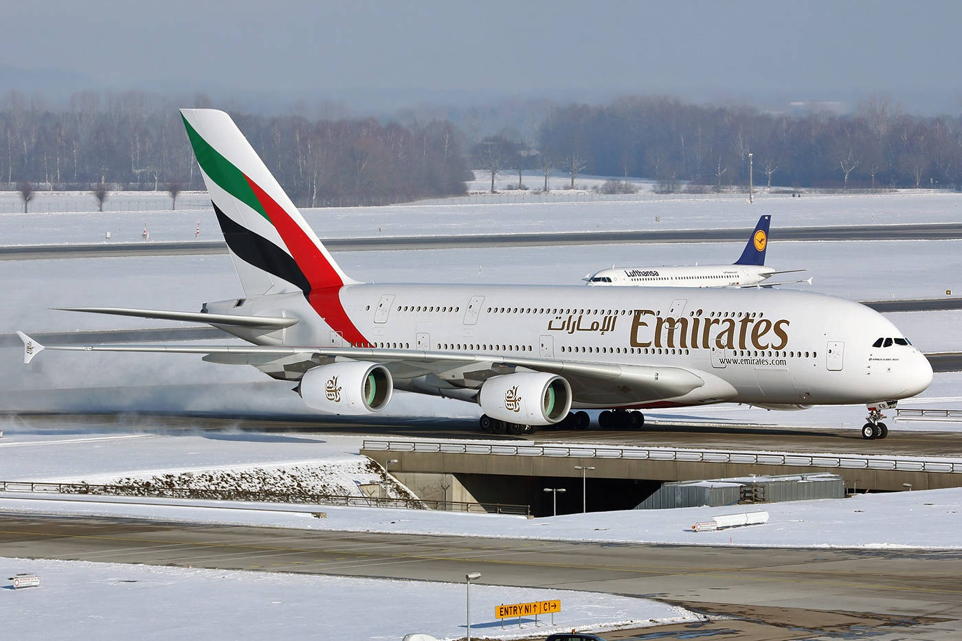 飛機 桌布 壁紙 — 一架阿聯酋航空的空中巴士A380在積雪覆蓋的跑道上滑行，背景中可見另一架飛機。