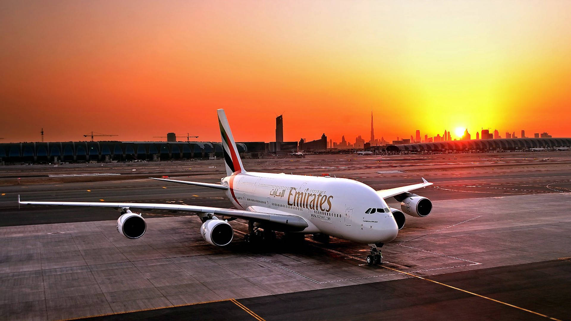 Airport 桌布 壁紙 — 一架阿聯酋航空空中巴士A380停在跑道上，夕陽在現代城市天際線後落下，投射出溫暖的橙色光芒。
